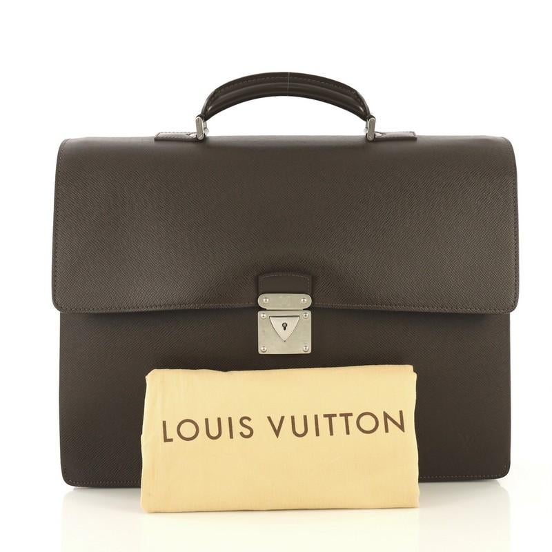 This Louis Vuitton Robusto 1 Briefcase Taiga Leather, crafted in brown taiga leather, features leather top handle with links, exterior back flat pocket, and silver-tone hardware. Its lock closure opens to a brown fabric interior with multiple open