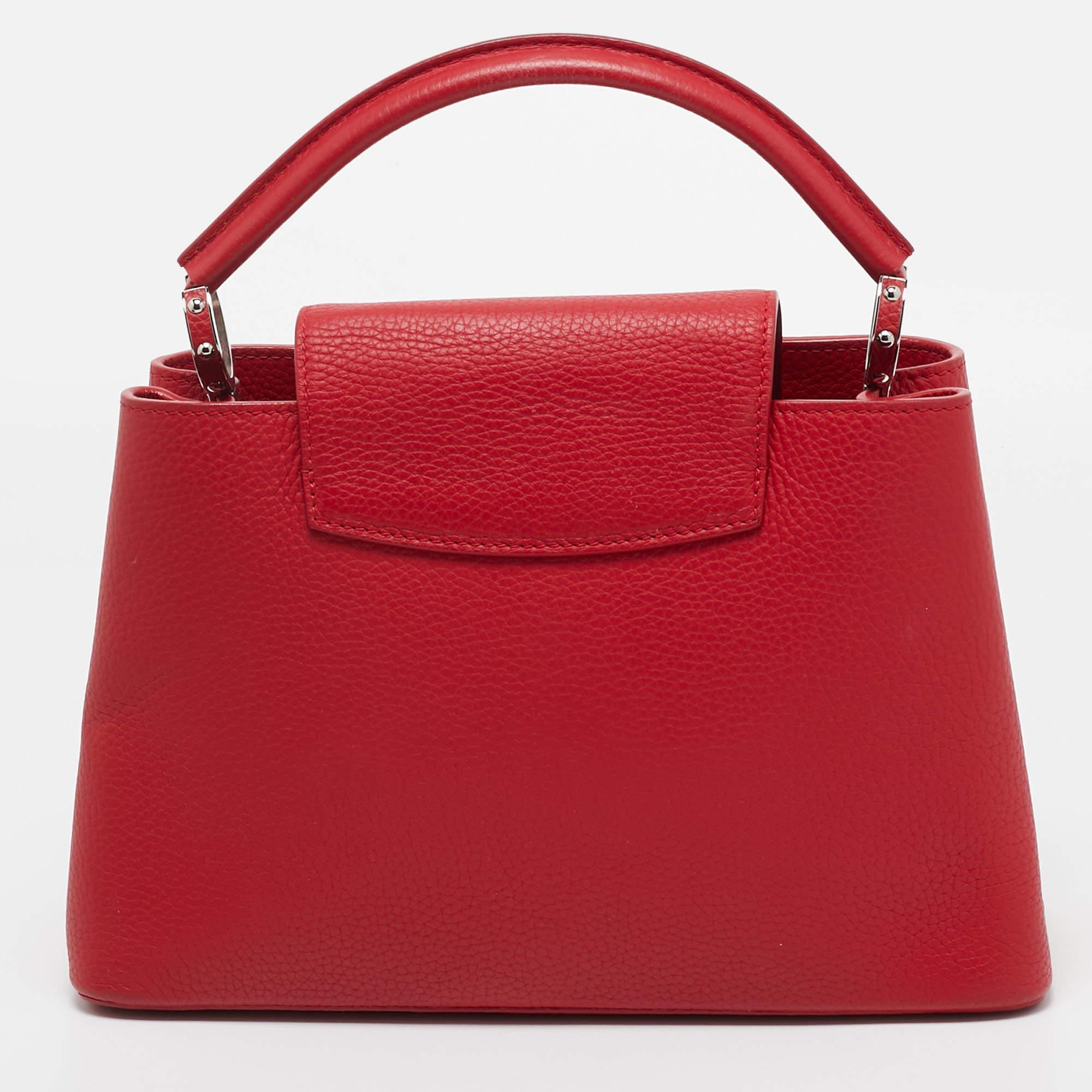 Die Louis Vuitton Capucines Tasche ist ein luxuriöses Accessoire aus exquisitem rubinrotem Taurillon-Leder. Sie verfügt über einen raffinierten Klappverschluss, doppelte Henkel und ein markantes LV-Monogramm. Das Innere ist mit feinem Leder