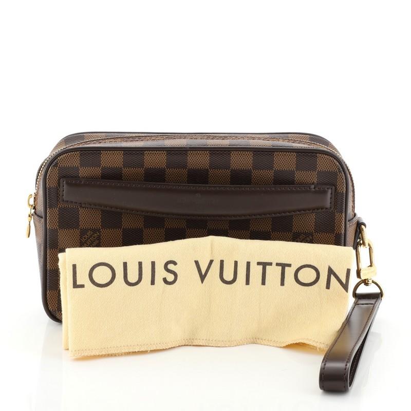 This Louis Vuitton Saint Paul Pochette Damier, crafted from Damier Ebene coated canvas, features a wrist strap, front handle and gold-tone hardware. Its zip closure opens to a brown fabric interior with multiple slip pockets. Authenticity code