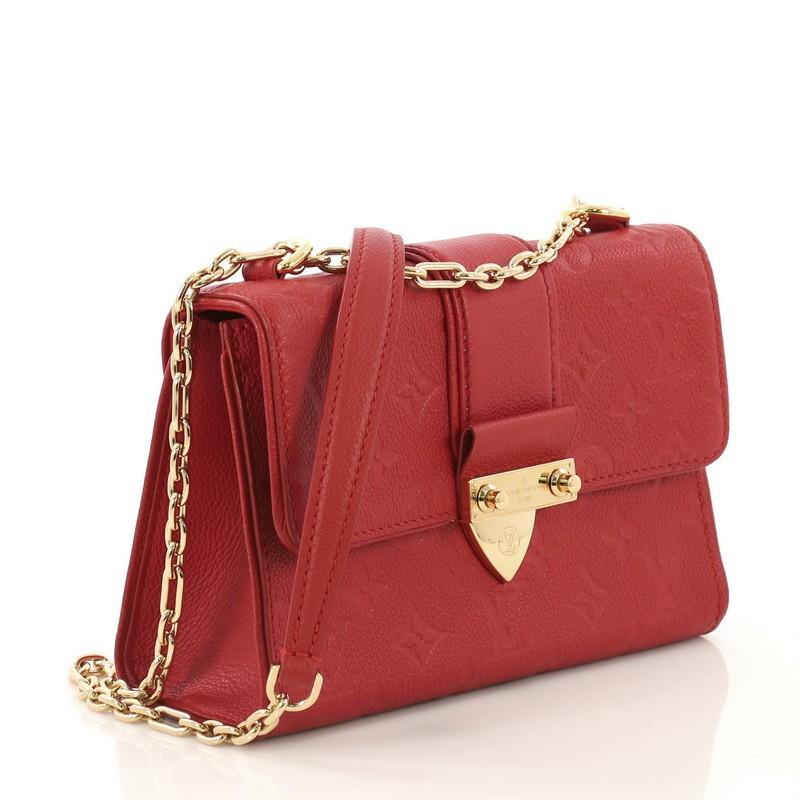 This Louis Vuitton Saint Sulpice Handbag Monogram Empreinte Leather BB, crafted in red monogram empreinte leather, features a sliding chain strap with leather shoulder pad, frontal flap, and gold-tone hardware. Its push-lock closure opens to a red