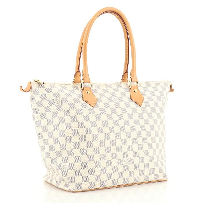 This Louis Vuitton Saleya Handbag Damier MM, crafted from damier azur coated canvas, features dual rolled vachetta leather tall handles and gold-tone hardware. Its zip closure opens to a neutral microfiber interior with slip pockets. Authenticity