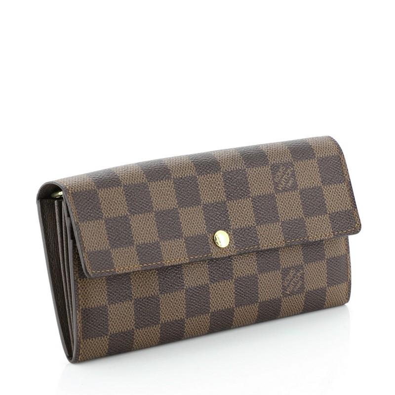 This Louis Vuitton Sarah Wallet Damier, crafted in damier ebene coated canvas, features gold-tone hardware. Its snap button closure opens to a brown leather interior with middle zip compartment and multiple card slots. Authenticity code reads: