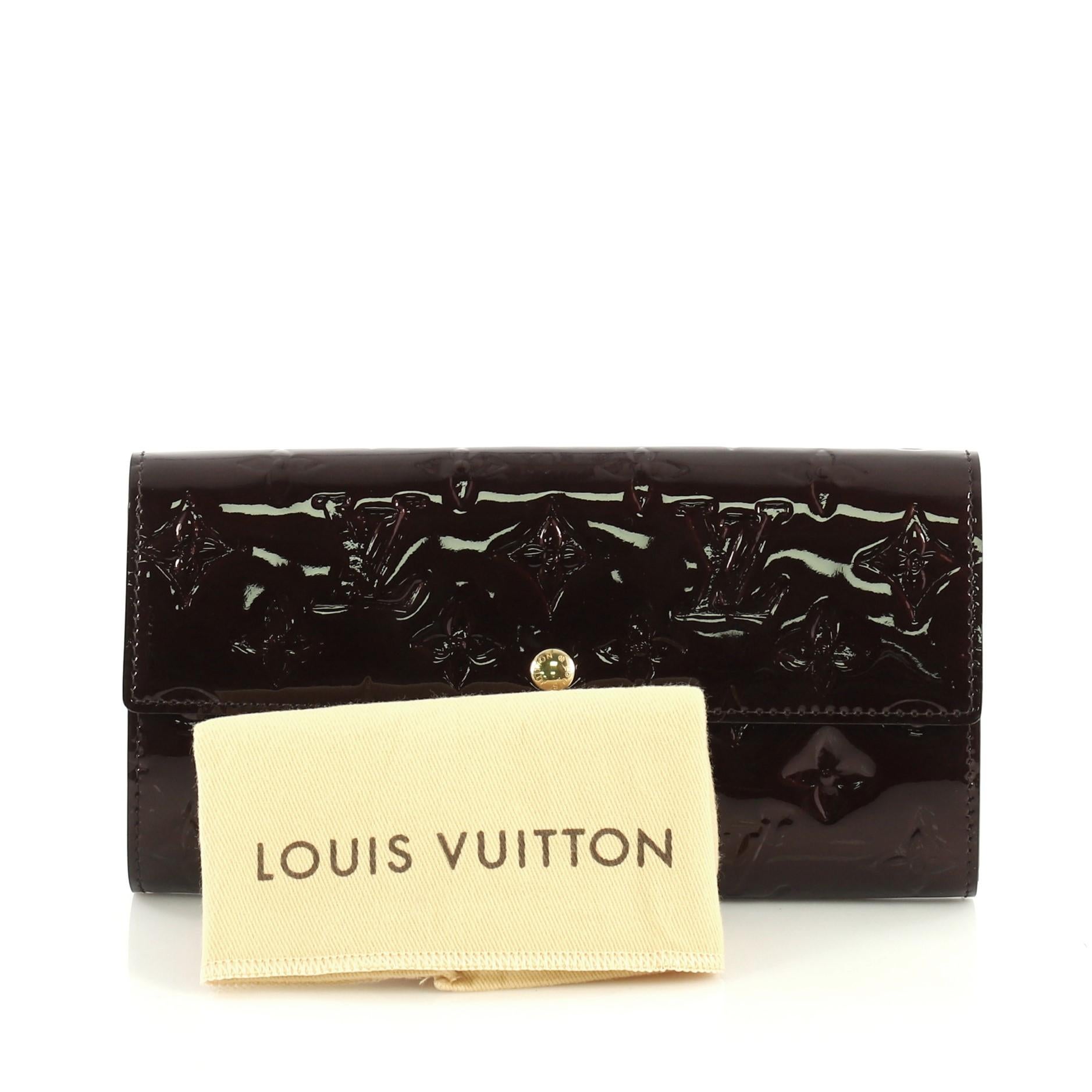 This Louis Vuitton Sarah Wallet Monogram Vernis, crafted in red monogram vernis leather, features gold-tone hardware. Its snap button closure opens to a purple leather interior with multiple card slots and a middle zip compartment. Authenticity code