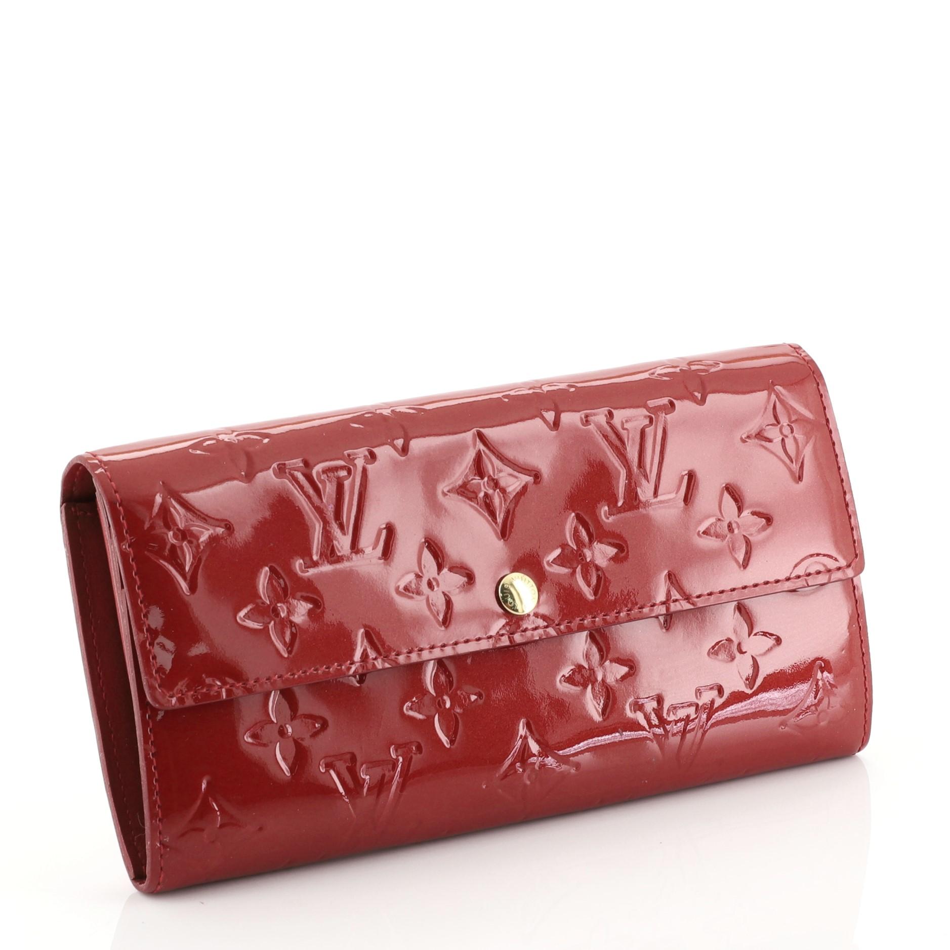This Louis Vuitton Sarah Wallet Monogram Vernis, crafted in red monogram vernis leather, features gold-tone hardware. Its snap button closure opens to a red leather interior with multiple card slots and a middle zip compartment. Authenticity code