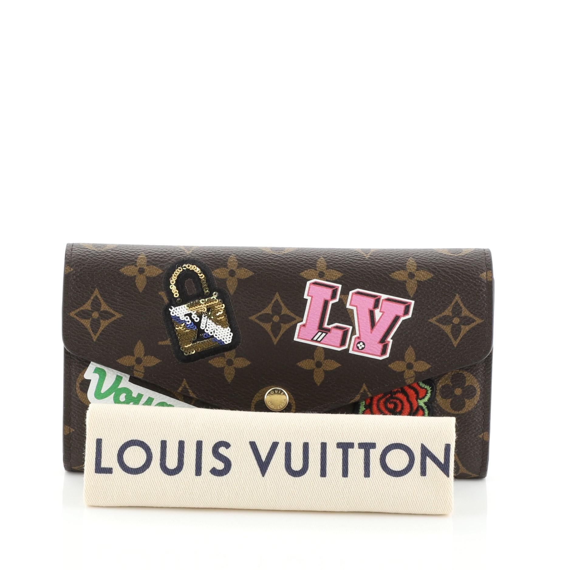 This Louis Vuitton Sarah Wallet NM Limited Edition Patches Monogram Canvas, crafted from brown monogram coated canvas, features an envelope-style frontal flap, multicolor patches, and gold-tone hardware. Its snap button closure opens to a pink