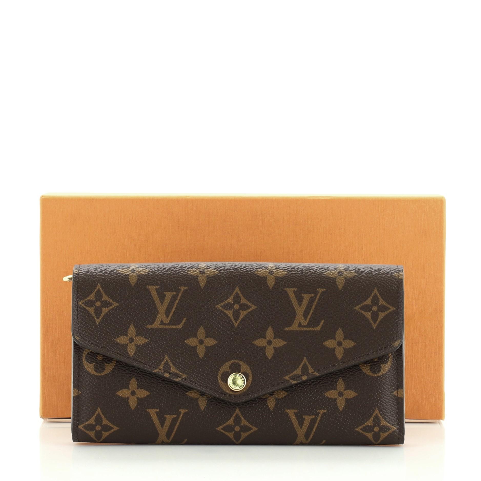 This Louis Vuitton Sarah Wallet NM Monogram Canvas, crafted in brown monogram coated canvas, features an envelope-style frontal flap and gold-tone hardware. Its snap button closure opens to a brown leather interior with multiple card slots and