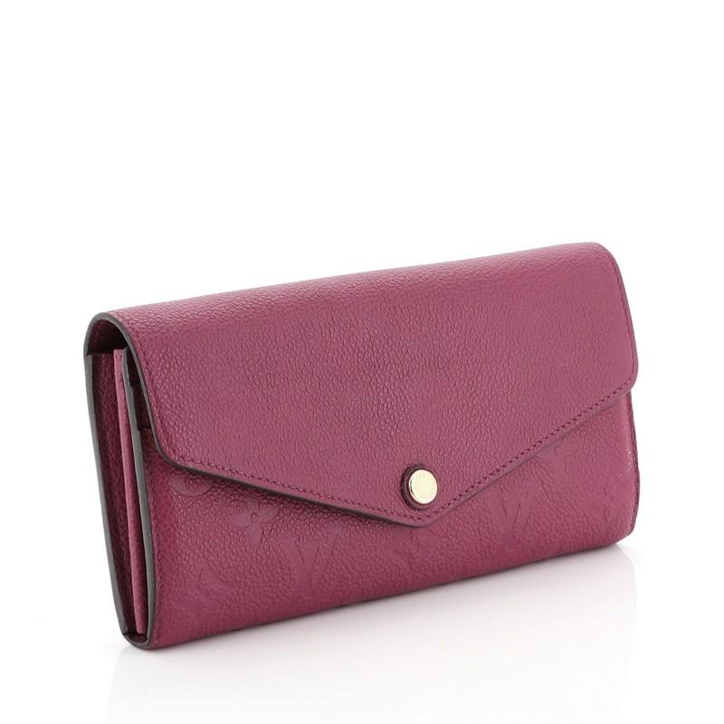This Louis Vuitton Sarah Wallet NM Monogram Empreinte Leather, crafted from purple monogram empreinte leather, features an envelope-style frontal flap and gold-tone hardware. Its snap button closure opens to a purple leather interior with multiple