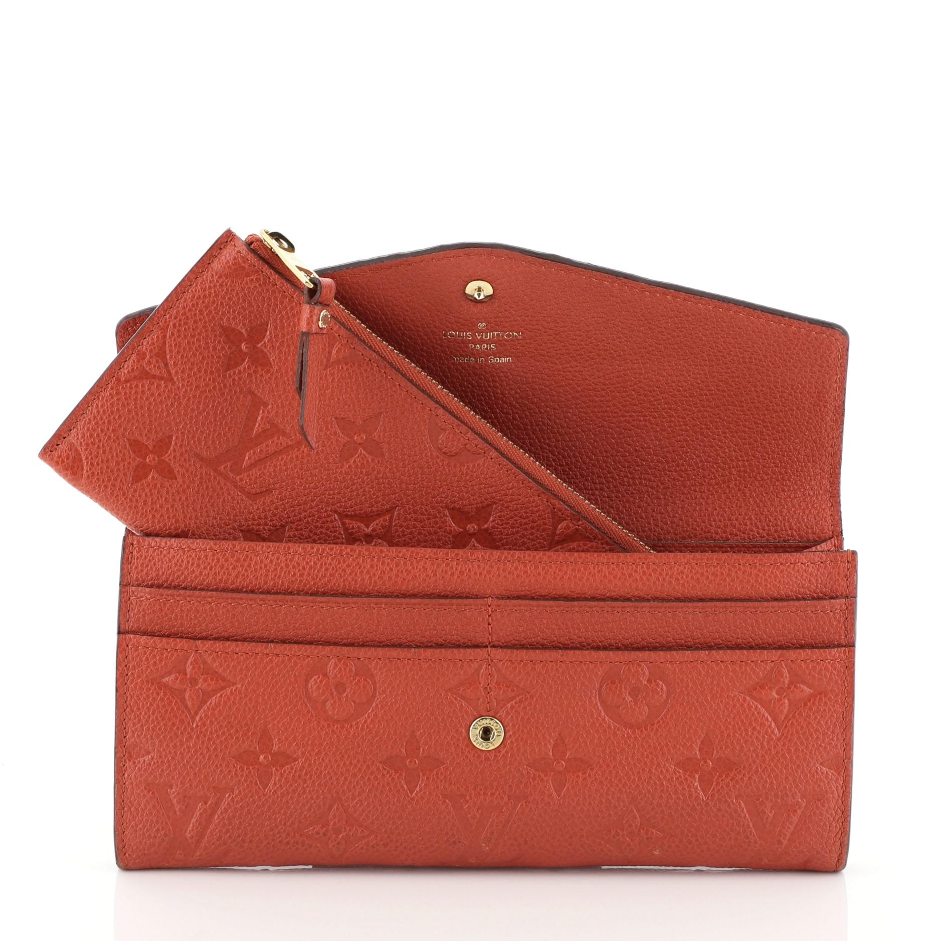 This Louis Vuitton Sarah Wallet NM Monogram Empreinte Leather crafted from red monogram empreinte leather, features an envelope-style frontal flap and gold-tone hardware. Its snap button closure opens to a red leather interior with multiple card