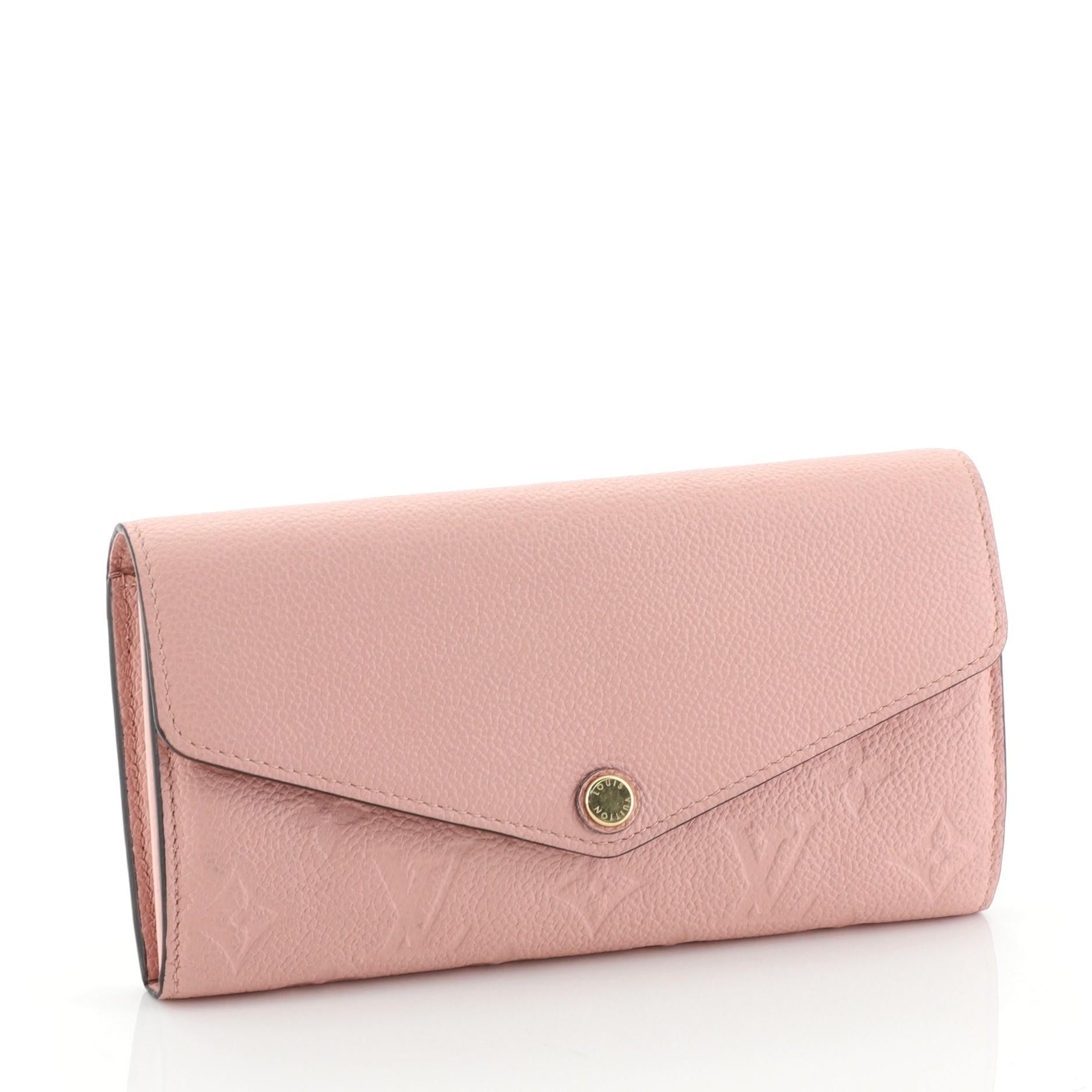 This Louis Vuitton Sarah Wallet NM Monogram Empreinte Leather, crafted from pink monogram empreinte leather, features an envelope-style frontal flap and gold-tone hardware. Its snap button closure opens to a pink leather interior with multiple card