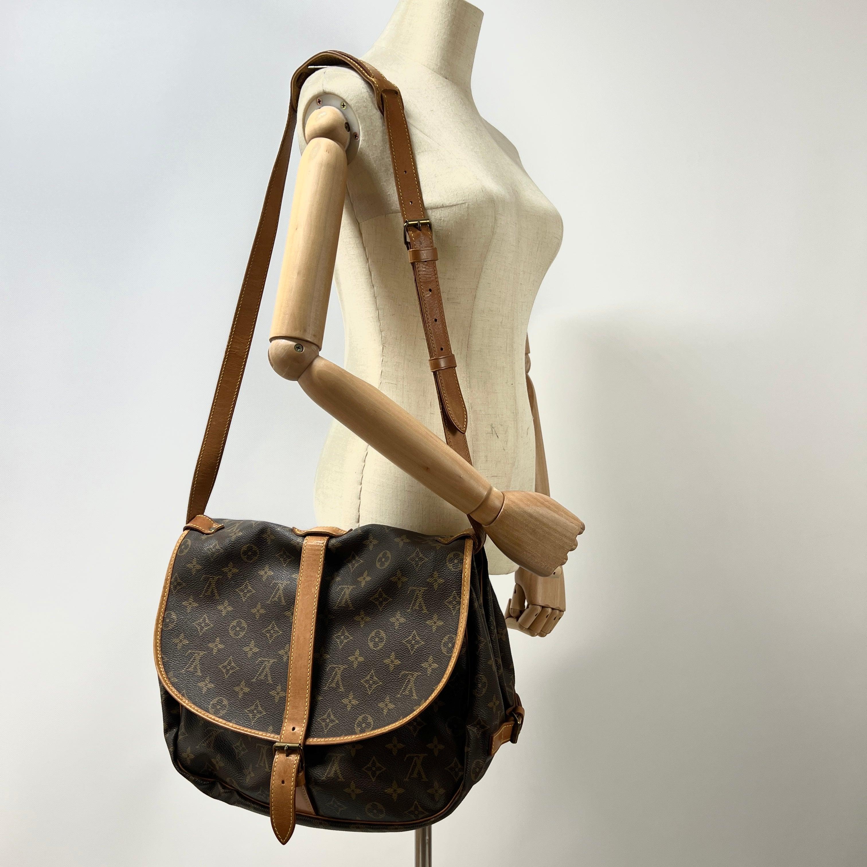 Saumur in monogram canvas with leather trim and gold-tone hardware. Twin compartments with buckle straps. Date code AR0990 (1990), France. Condition: good with leather creasing and micro scratches to leather and hardware. Dimensions: 35 × 26 × 20 cm.