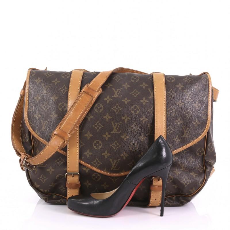 This Louis Vuitton Saumur Handbag Monogram Canvas 43, crafted in brown monogram coated canvas, features a long adjustable strap, double saddle compartments with side buckle vachetta leather closures at its frontal flaps, and gold-tone hardware. Its