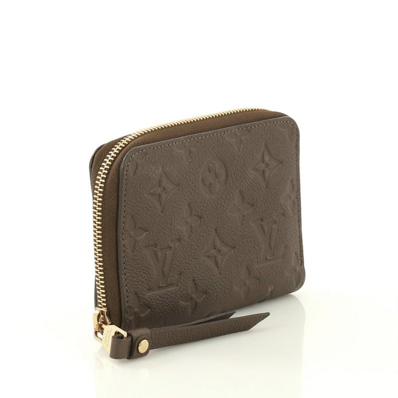 This Louis Vuitton Secret Wallet Monogram Empreinte Leather Compact, crafted from brown monogram empreinte leather, features gold-tone hardware. Its zip around closure opens to a brown leather interior with multiple card slots and slip and zip
