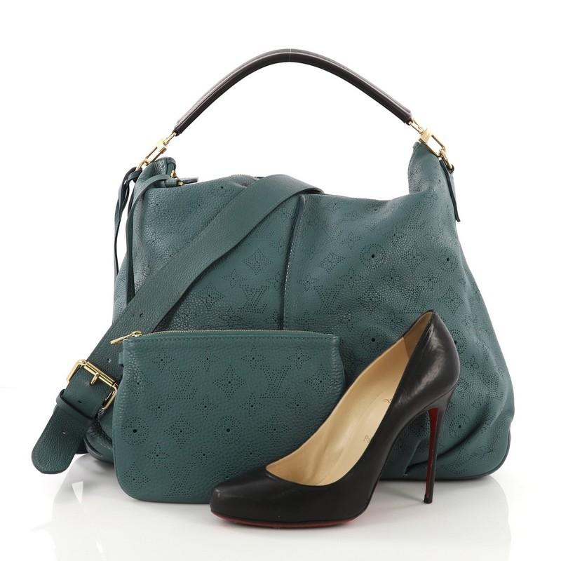 This Louis Vuitton Selene Handbag Mahina Leather MM, crafted from teal monogram perforated mahina leather, features a flat top handle, pleated detailing, and gold-tone hardware. Its top zip closure opens to a dark gray microfiber interior with side