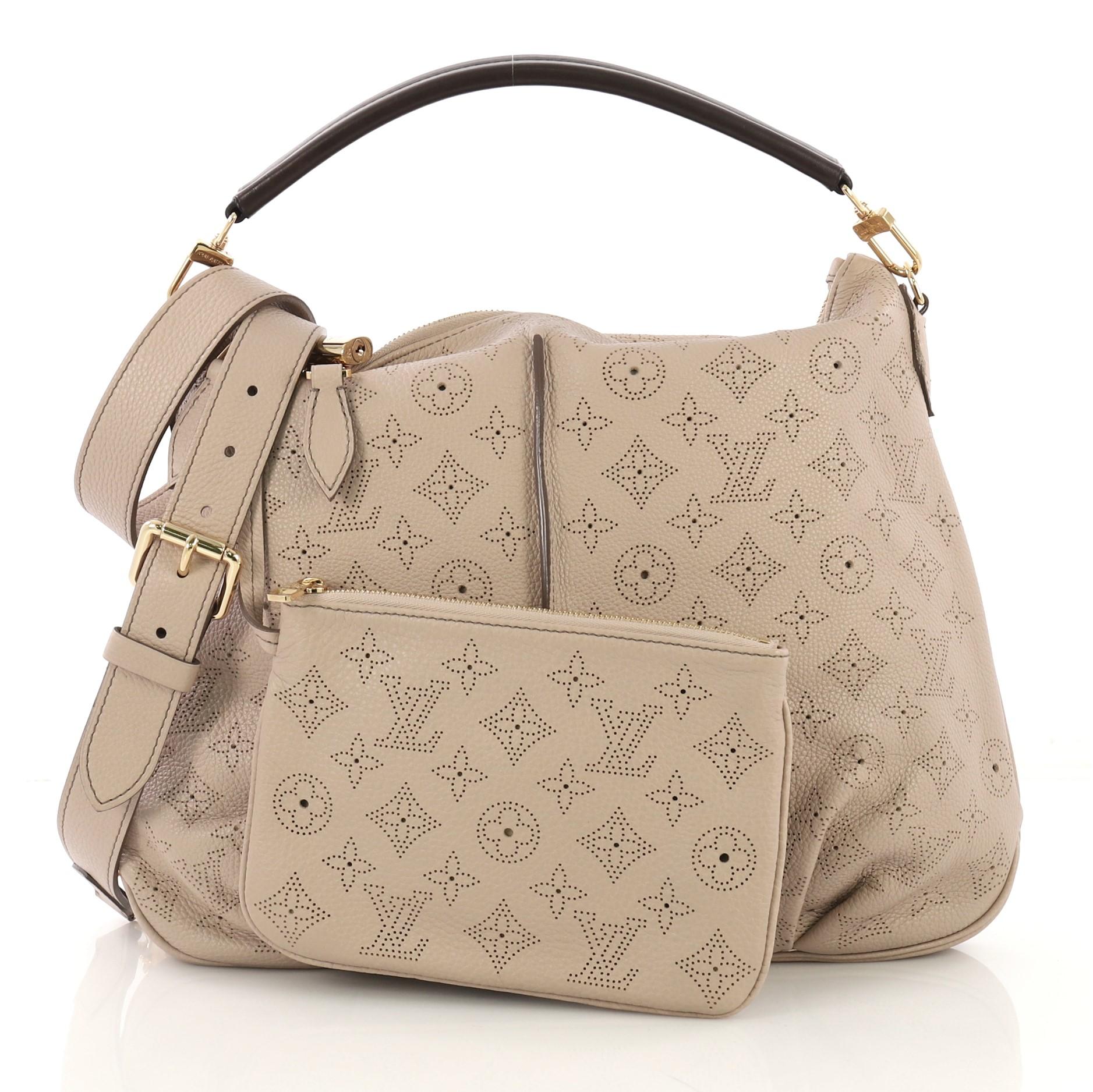 This Louis Vuitton Selene Handbag Mahina Leather PM, crafted from beige monogram perforated mahina leather, features a leather handle, pleated detailing, and gold-tone hardware. Its zip closure opens to a brown microfiber interior with side zip and