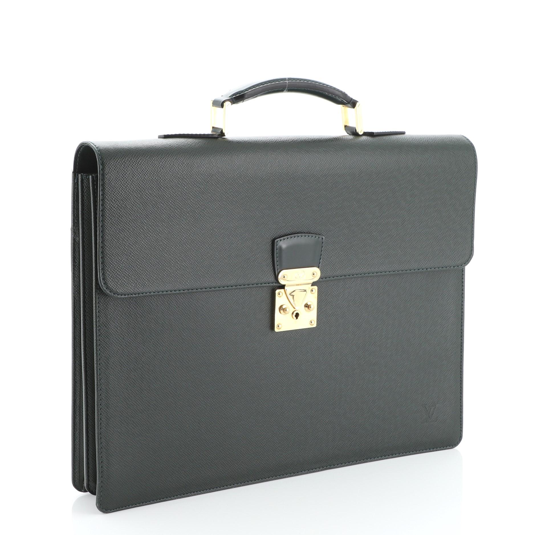 This Louis Vuitton Serviette Moskova Briefcase Taiga Leather, crafted in green taiga leather, features a leather top handle, exterior back flat pocket, and gold-tone hardware. Its S-lock closure opens to a green leather interior divided into two