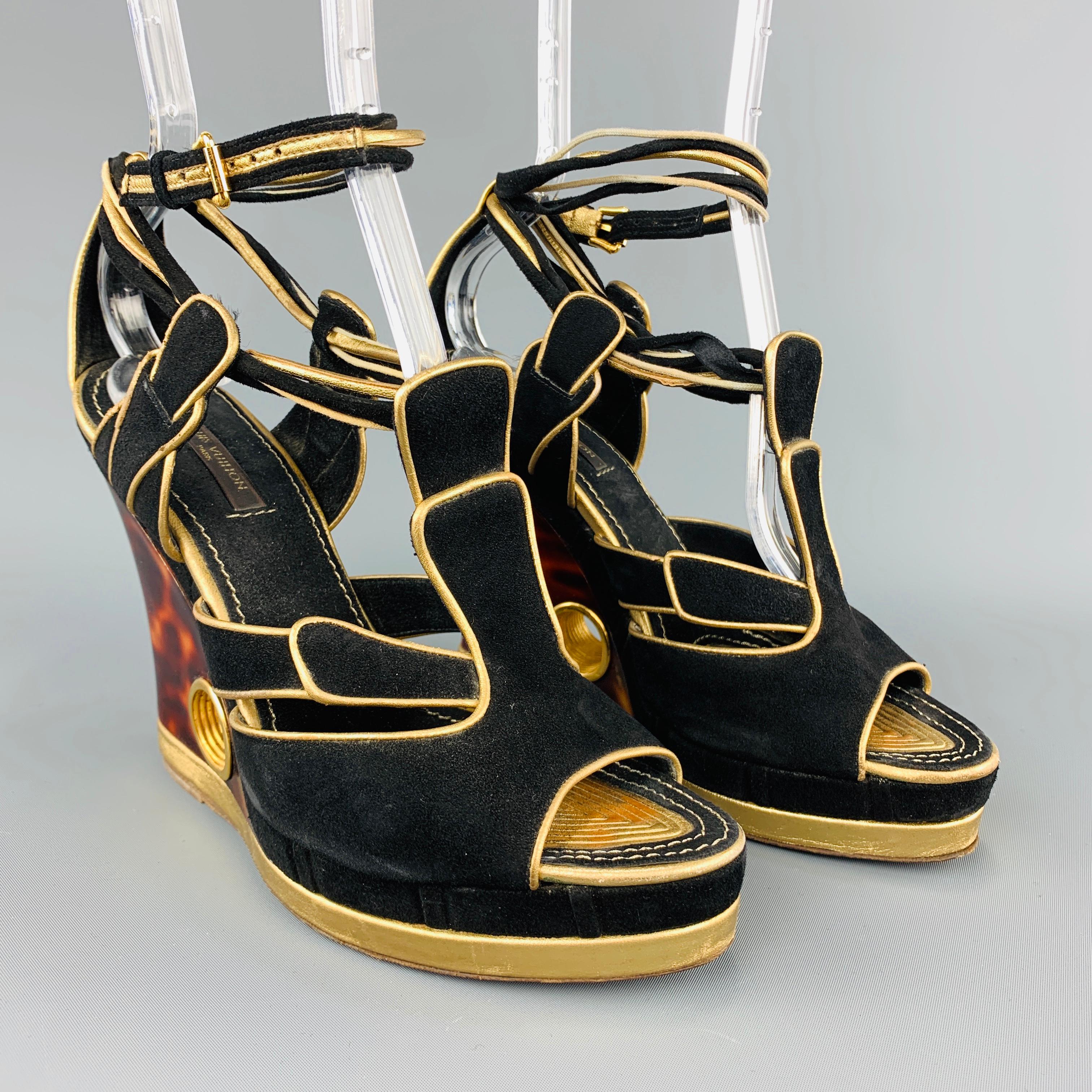 LOUIS VUITTON sandals come in black suede with metallic gold leather piping, peep toe and cutouts, and acrylic tort print wedge heel with gold tone metal cutout. Wear through out. Made in Italy.
 
Good Pre-Owned Condition.
Marked: IT 37
 
Heel: 4.5