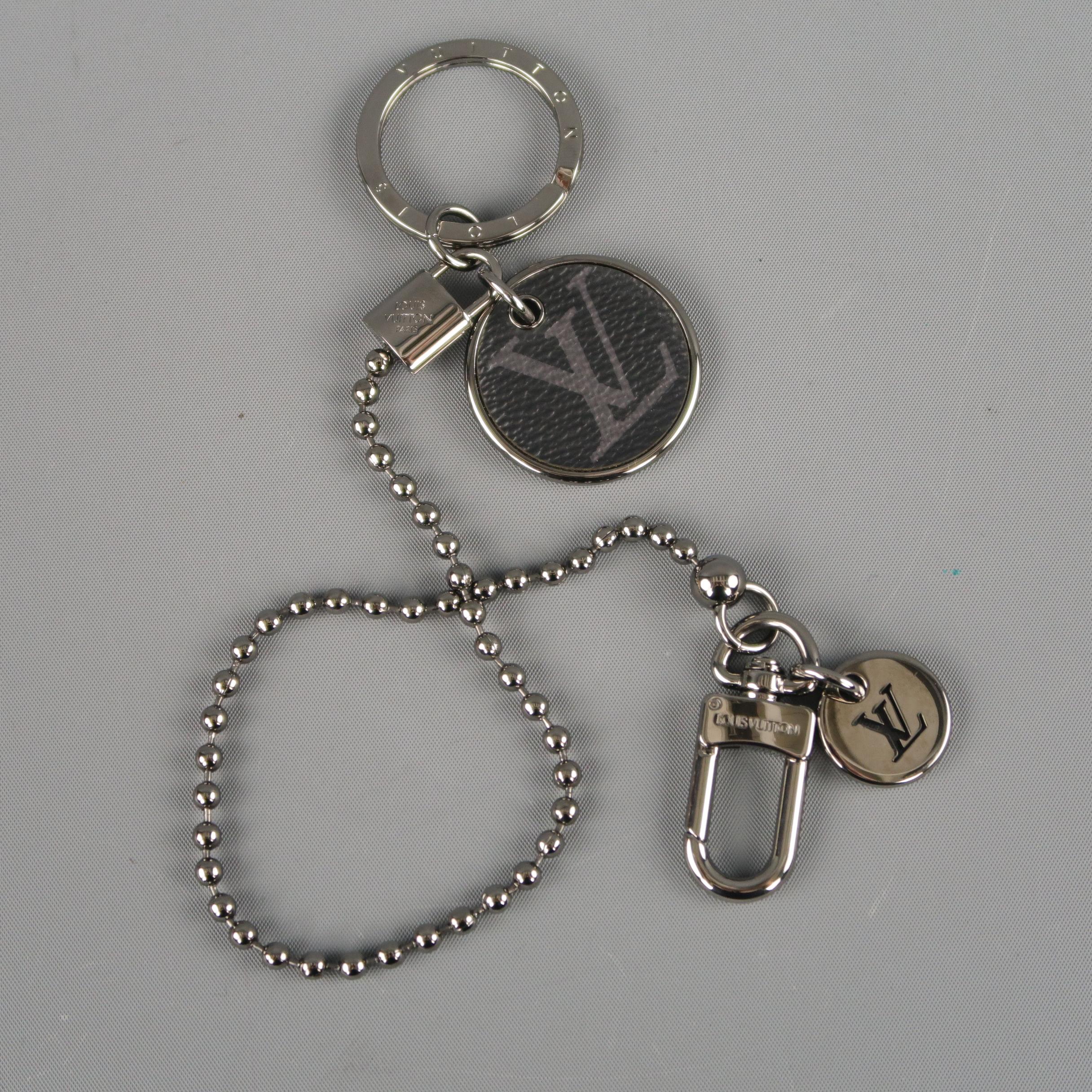 LOUIS VUITTON wallet key chain comes in smoke silver tone metal and features a ball chain with a LV monogram cutout charm and clasp on one side and mock lock, embossed key loop, and gray canvas charm on the other. With box. Made in Italy.
