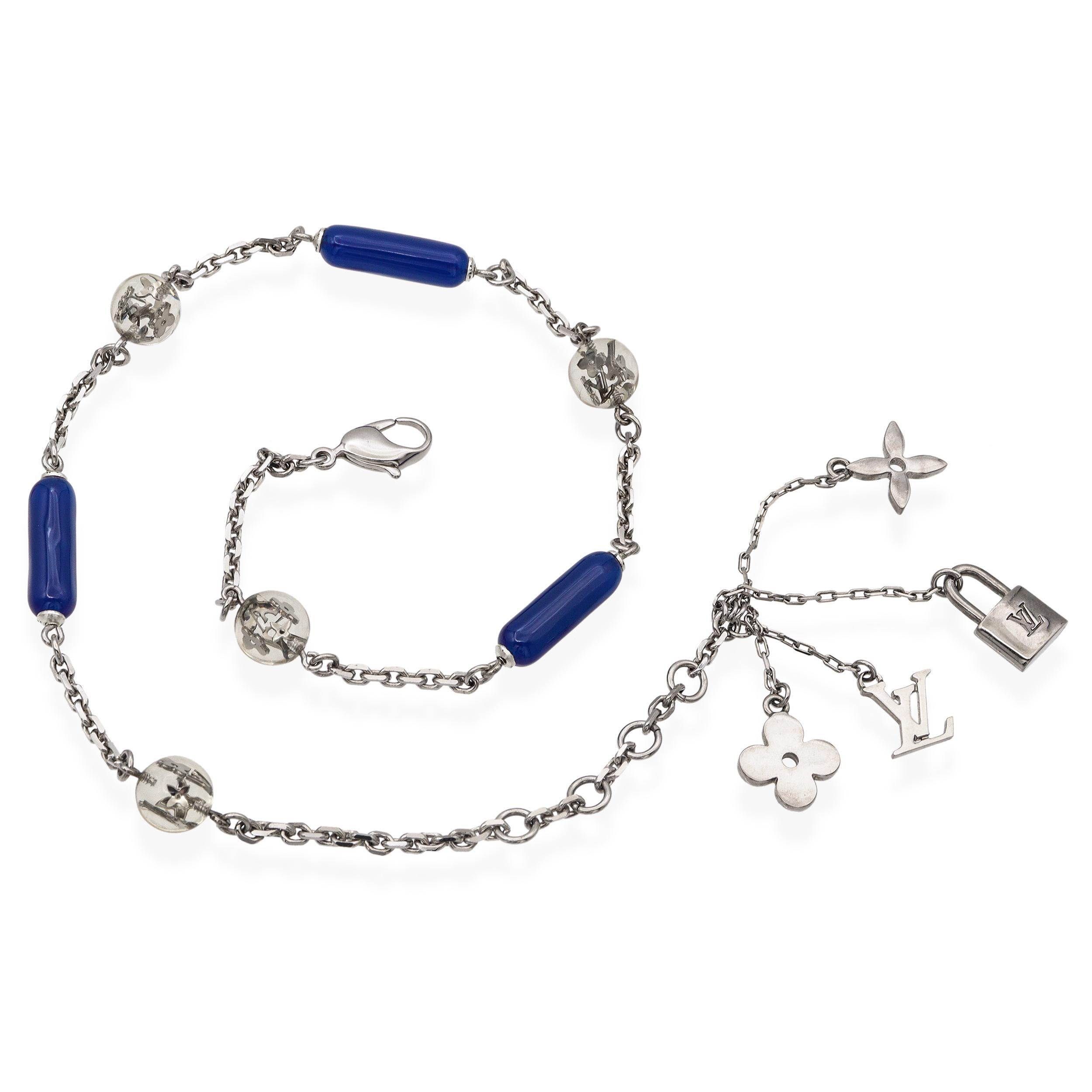Ce ravissant collier Louis Vuitton allie un métal argenté élégant à des touches de bleu vibrant dans une chaîne sinueuse. Il est orné de perles cylindriques bleues et de charmes emblématiques, comme un cadenas élégant, suspendus le long de la chaîne
