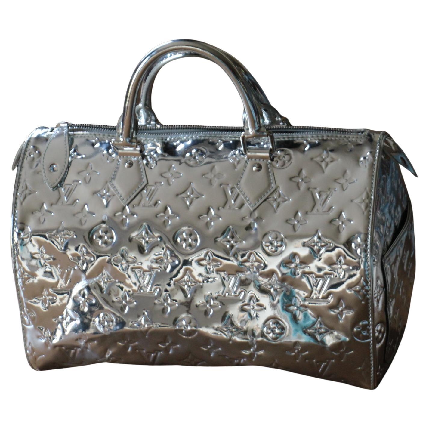  This Louis Vuitton Speedy 35 Silver Monogram Miroir Handbag Purse is an extremely rare and limited edition . It features ultra-shiny monogram mirrored vinyl with patent leather trim and a  silver tone padlock and keys to lock up all your precious