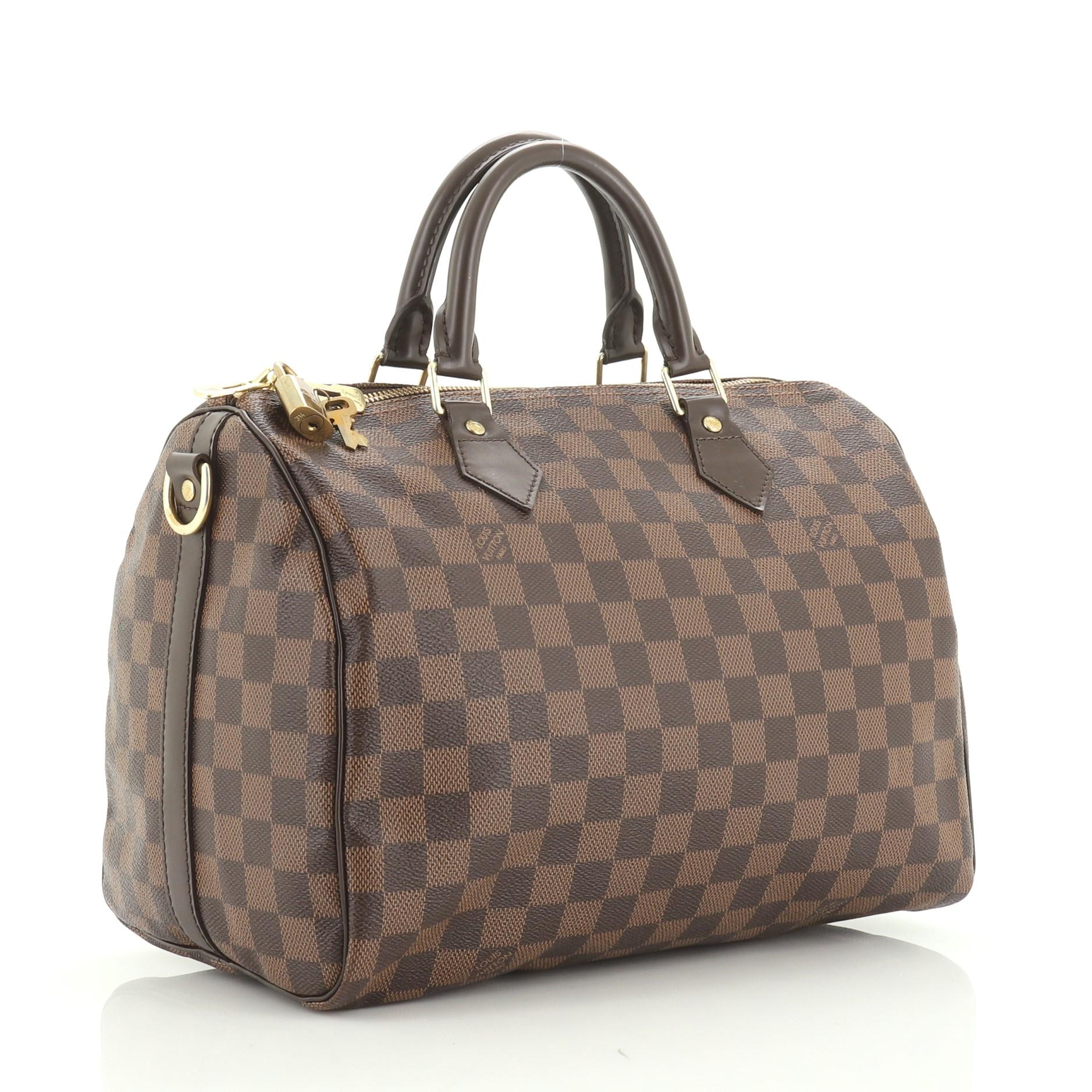 This Louis Vuitton Speedy Bandouliere Bag Damier 30, crafted in damier ebene coated canvas, features dual rolled handles, leather trim, and gold-tone hardware. Its zip closure opens to a red fabric interior with zip pocket. Authenticity code reads: