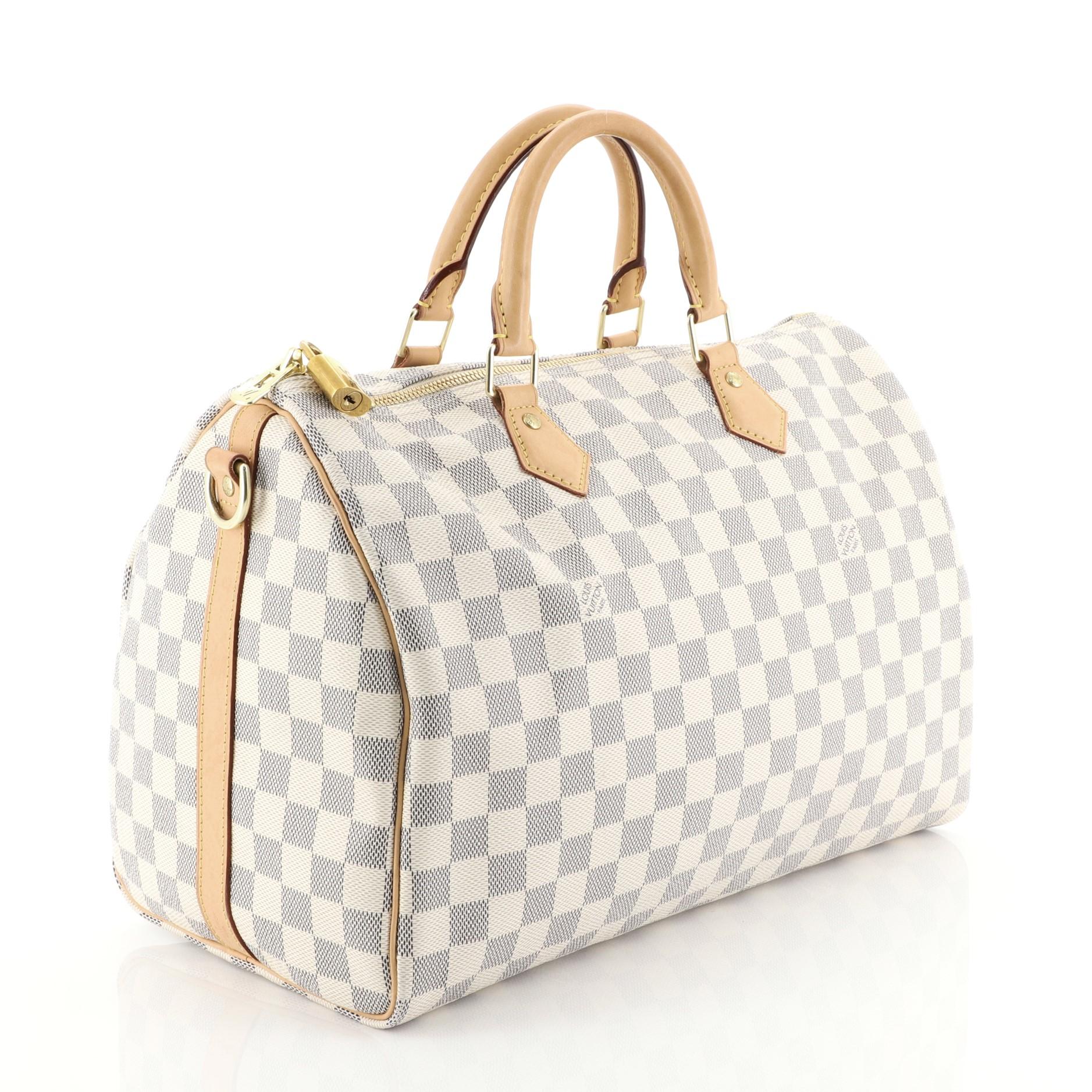 This Louis Vuitton Speedy Bandouliere Bag Damier 35, crafted from damier azur coated canvas, features dual rolled handles, leather trim and gold-tone hardware. Its two-way zip closure opens to a neutral fabric interior with slip pocket. Authenticity