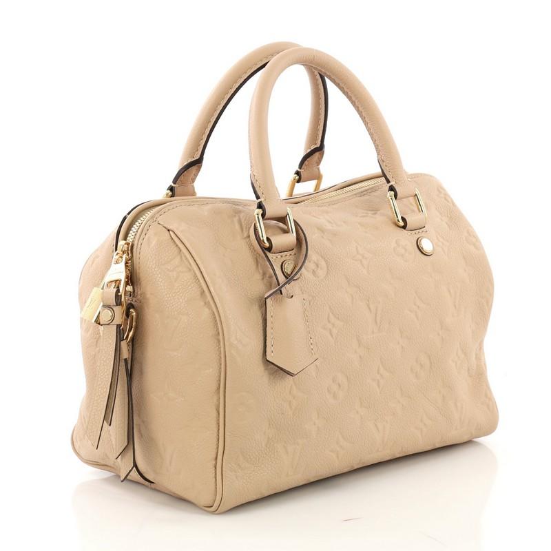 This Louis Vuitton Speedy Bandouliere Bag Monogram Empreinte Leather 25, crafted from nude monogram embossed empreinte leather, features dual rolled leather handles, protective base studs, and gold-tone hardware. Its two-way zip closure opens to a