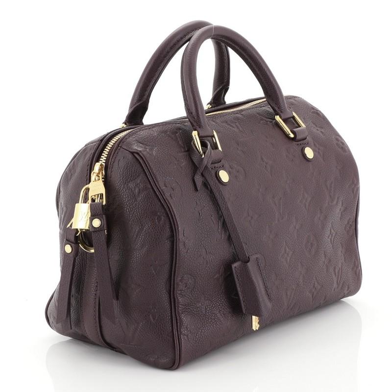This Louis Vuitton Speedy Bandouliere Bag Monogram Empreinte Leather 25, crafted from purple monogram empreinte leather, features dual rolled leather handles, protective base studs, and gold-tone hardware. Its two-way zip closure opens to a purple