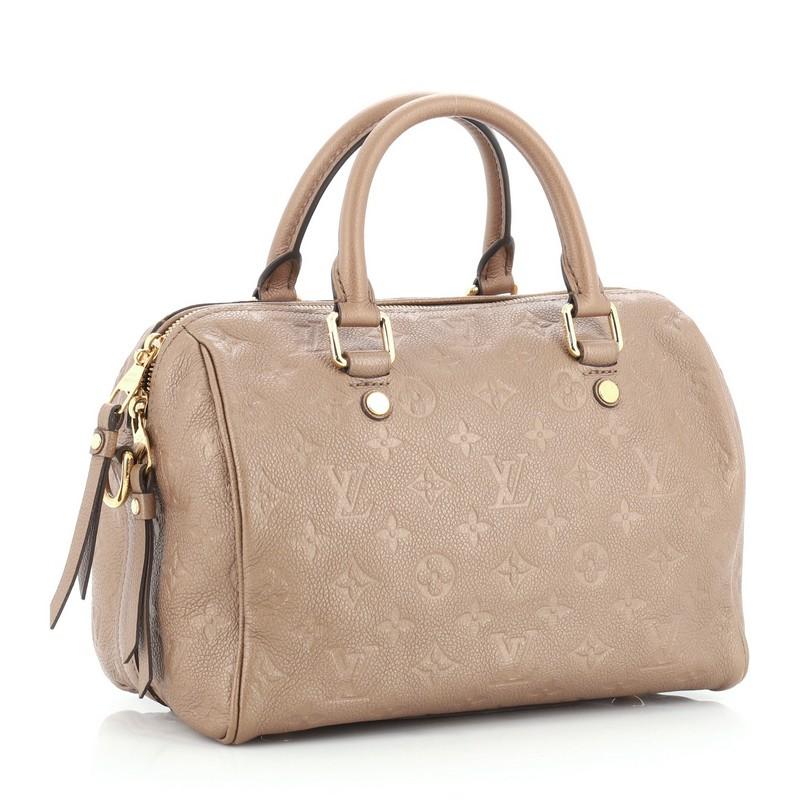 This Louis Vuitton Speedy Bandouliere Bag Monogram Empreinte Leather 25, crafted from neutral monogram empreinte leather, features dual rolled leather handles, protective base studs, and gold-tone hardware. Its two-way zip closure opens to a neutral