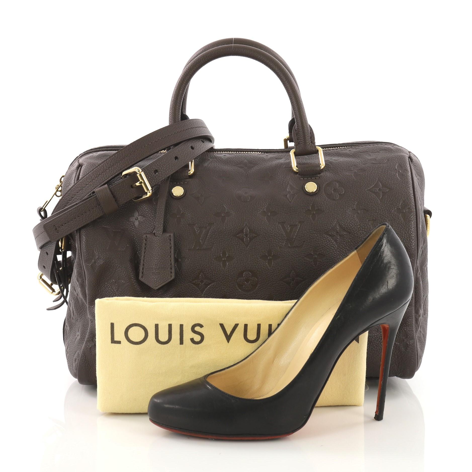 This Louis Vuitton Speedy Bandouliere Bag Monogram Empreinte Leather 30, crafted in brown monogram empreinte leather, features dual rolled leather handles, protective base studs, and gold-tone hardware. Its zip closure opens to a brown fabric