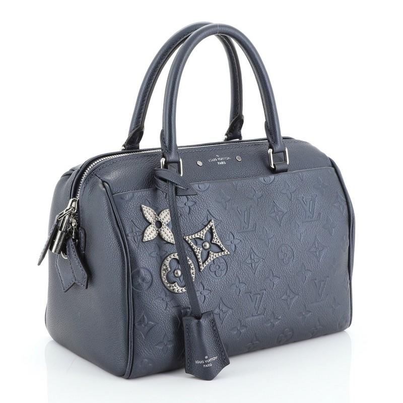 This Louis Vuitton Speedy Bandouliere NM Handbag Pins Monogram Empreinte Leather 25, crafted from blue monogram empreinte leather, features dual rolled leather handles, monogram metal flower pins and aged silver-tone hardware. Its two-way zip