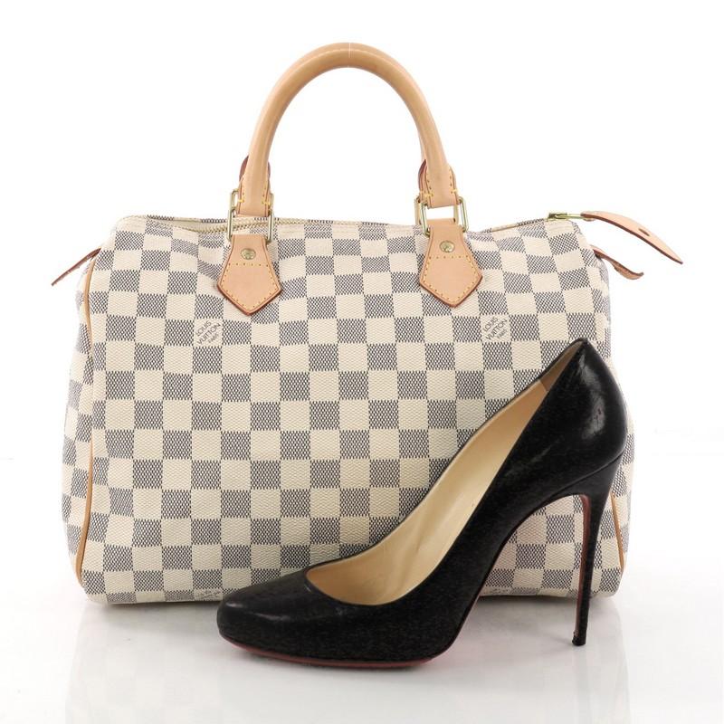 This Louis Vuitton Speedy Handbag Damier 30, crafted in damier azur coated canvas, features dual rolled handles, vachetta leather trims, and gold-tone hardware. Its top zip closure opens to a beige fabric interior with slip pocket. Authenticity code