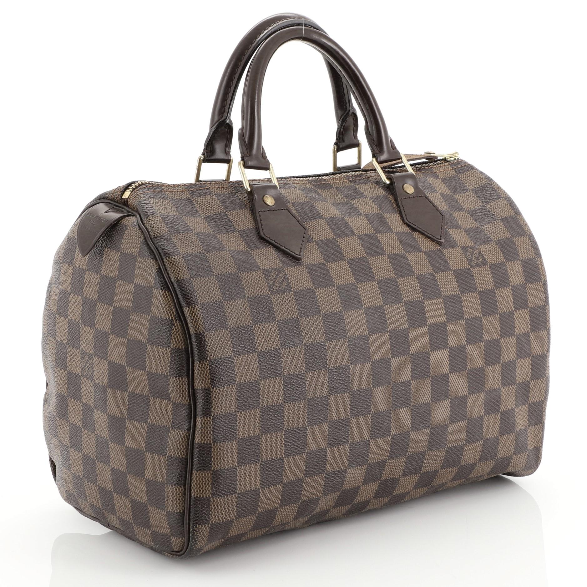 This Louis Vuitton Speedy Handbag Damier 30, crafted in damier ebene coated canvas, features dual rolled handles, leather trim, and gold-tone hardware. Its zip closure opens to a red fabric interior with slip pocket. Authenticity code reads: SP1087.