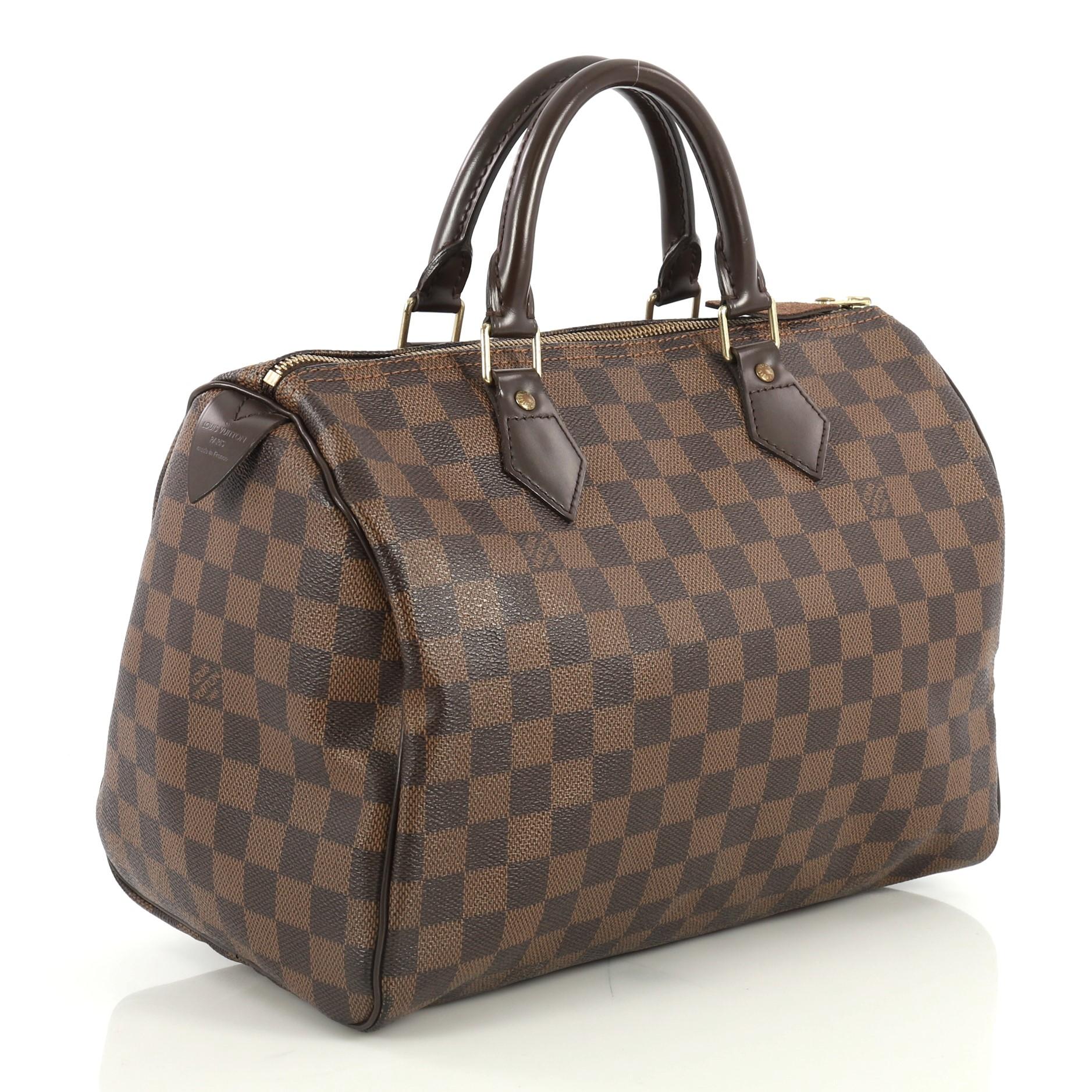 This Louis Vuitton Speedy Handbag Damier 30, crafted in damier ebene coated canvas, features dual rolled handles, leather trim, and gold-tone hardware. Its zip closure opens to a red fabric interior with slip pocket. Authenticity code reads: SP1026.