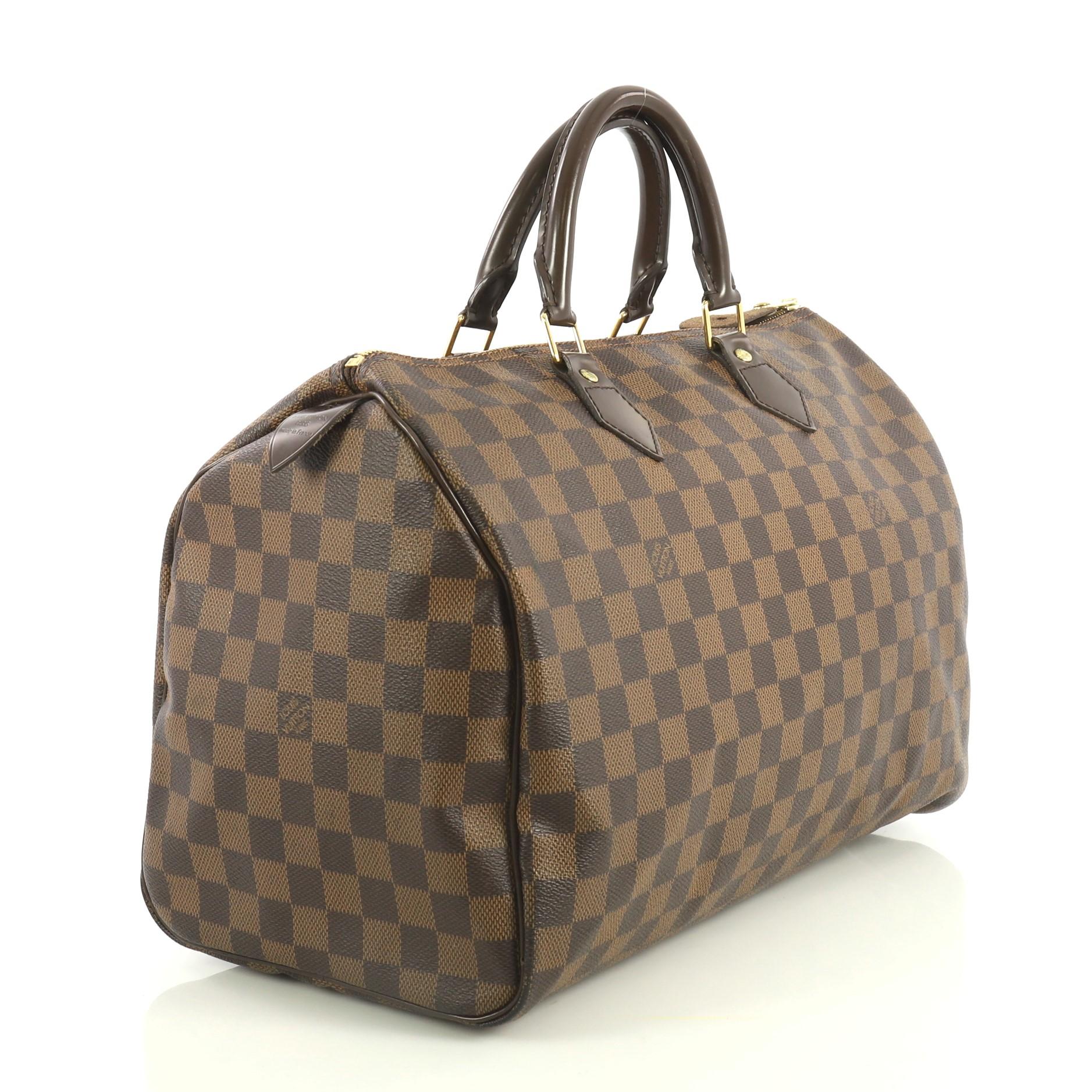 This Louis Vuitton Speedy Handbag Damier 35, crafted in damier ebene coated canvas, features dual rolled handles, leather trim and gold-tone hardware. Its zip closure opens to a red fabric interior with slip pocket. Authenticity code reads: TR4153.