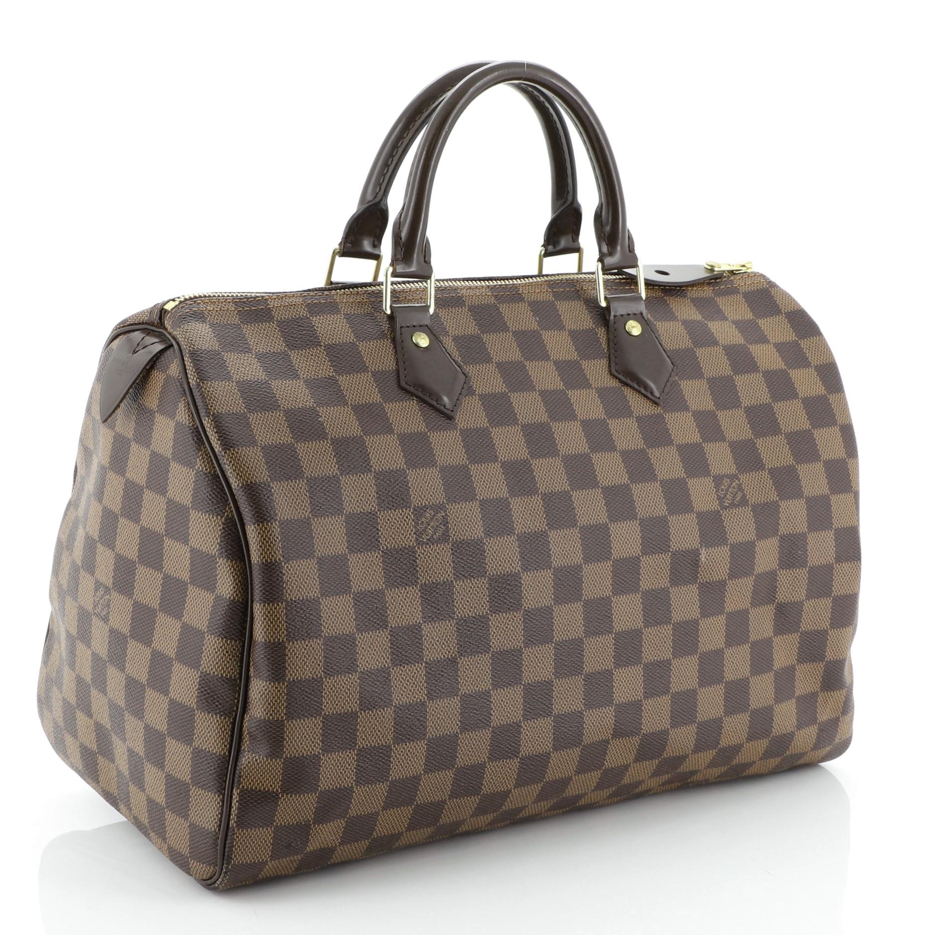 This Louis Vuitton Speedy Handbag Damier 35, crafted in damier ebene coated canvas, features dual rolled handles, leather trim and gold-tone hardware. Its zip closure opens to a red fabric interior with slip pocket. Authenticity code reads: SD2165.