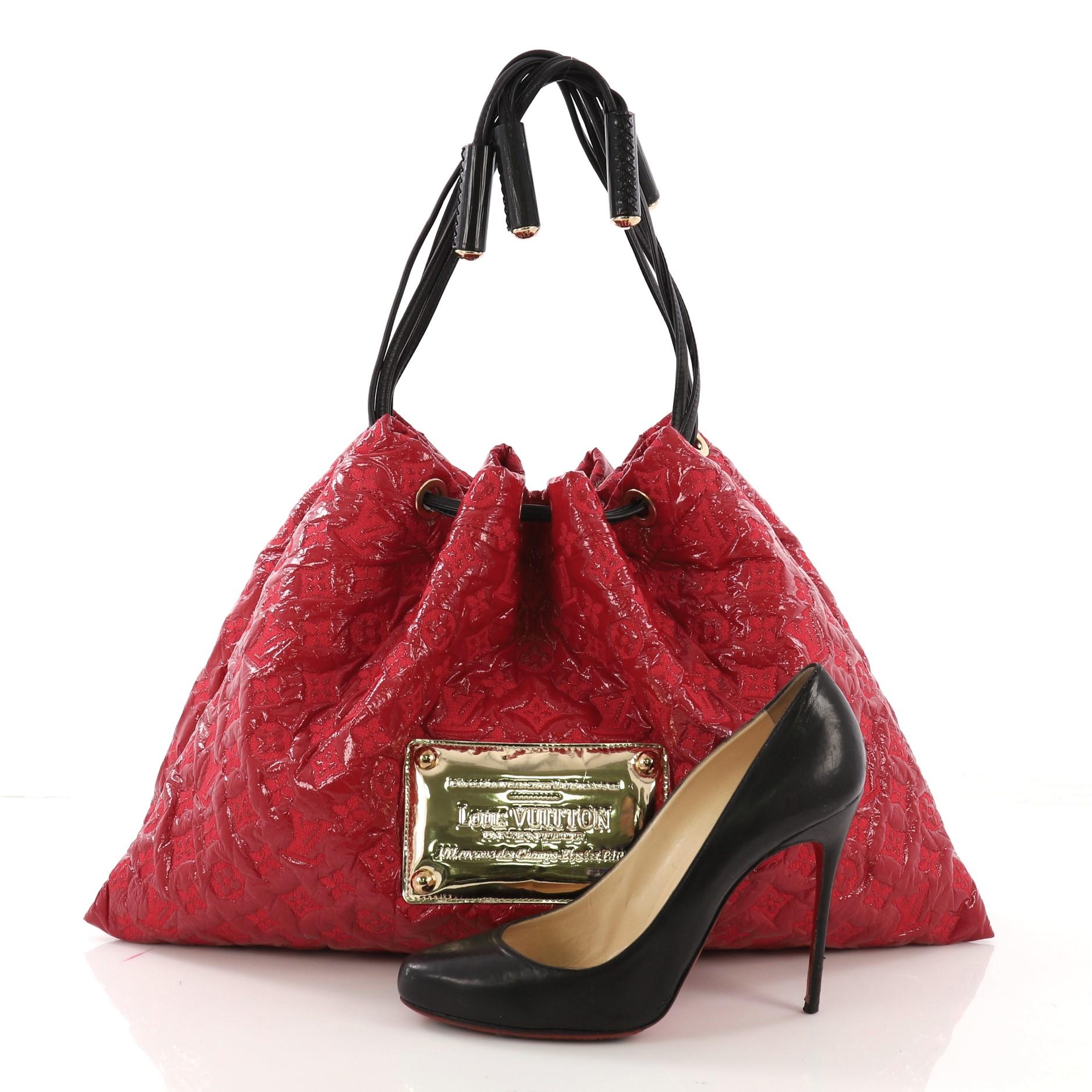 This Louis Vuitton Squishy Tote Monogram Vinyl, crafted in red monogram vinyl, features a gold plated LV logo at the center, contrasting black leather cinch cords threaded through rivets, and gold-tone hardware. Its drawstring closure opens to a
