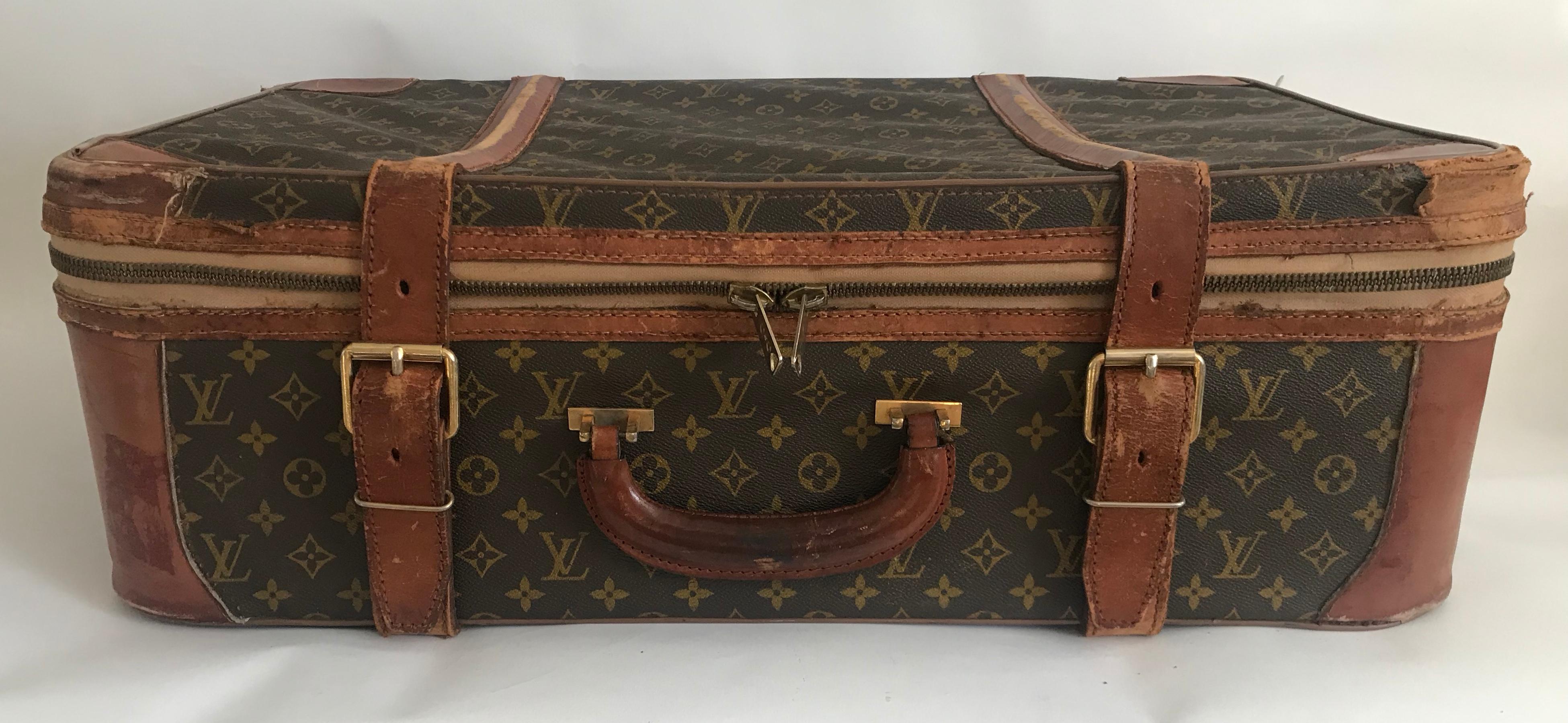 Brown and beige leather and canvas monogram suitcase from Louis Vuitton Vintage featuring a round top handle, a hanging luggage tag, buckle fastenings, a monogram print, leather trims, elasticated internal side pockets and internal buckle straps.
 