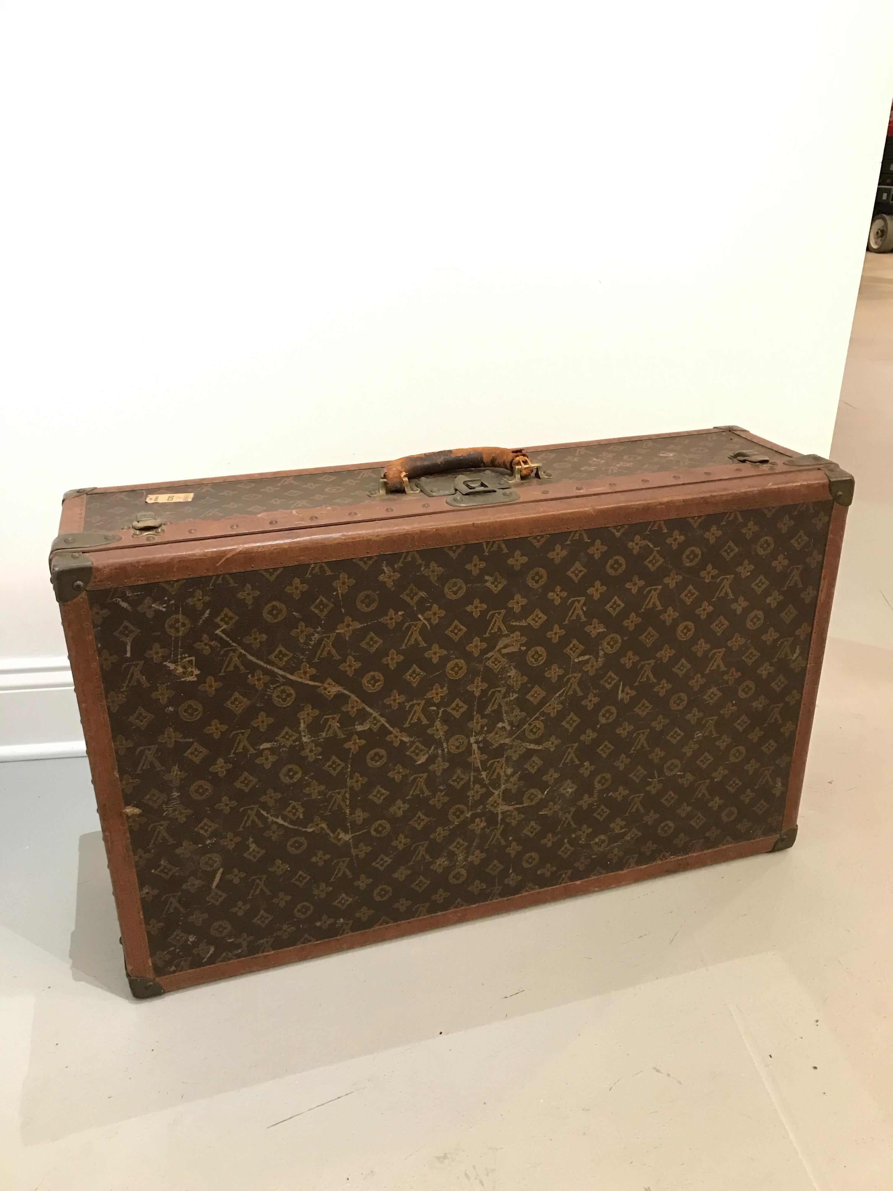 French, 20th century. A Louis Vuitton suitcase with a monogram canvas exterior, leather and brass-bound (all rivets and hardware are marked), opens to fitted interior with removable tray, labeled on interior lid with stamped serial number 773450 and