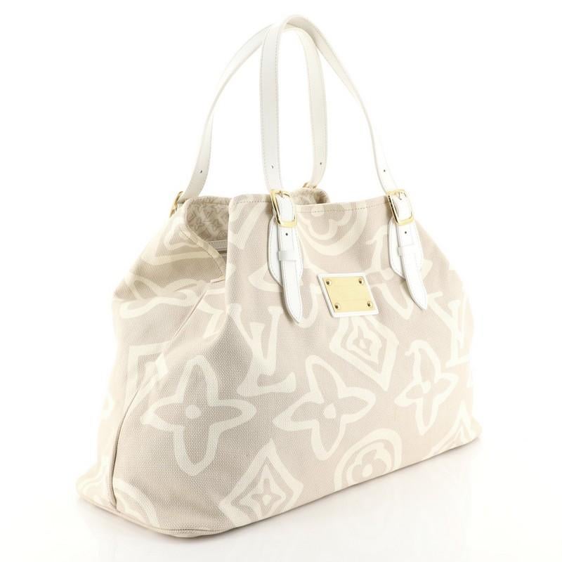 This Louis Vuitton Tahitienne Cabas Canvas GM, crafted in neutral canvas, features adjustable leather handles with buckle detailing, Louis Vuitton Inventeur plated logo, and gold-tone hardware. Its wide top opening displays a neutral fabric interior