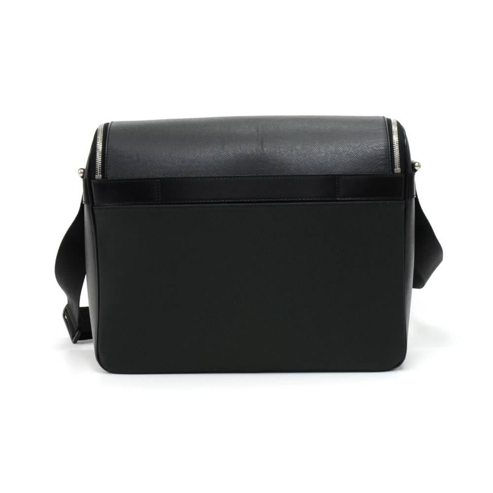 Louis Vuitton Taimyr messenger bag in black Taiga leather. It has a flap with a double zipper in the front and 1 open pocket on the back. The back has a strip of leather to allow you to slide your bag through suitcase handles to stack it on top.