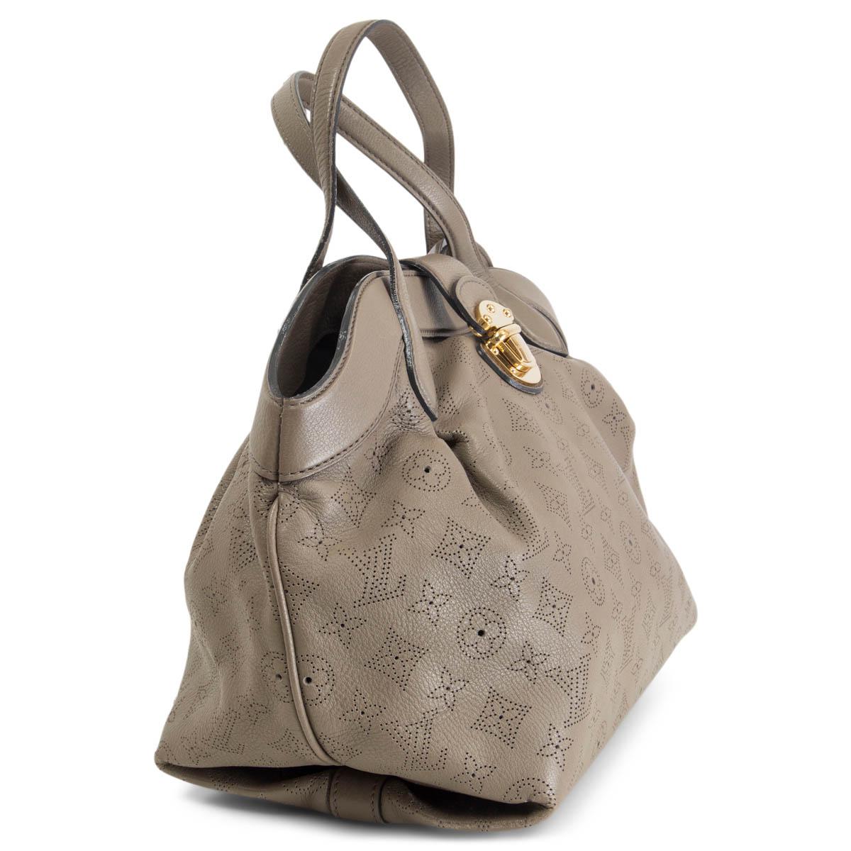 100% authentic Louis Vuitton PM Cirrus Mahina Handbag in taupe perforated Monogram Mahina leather. The push lock closure opens to a black alcantara lined interior with one zip pocket against the back and two open pockets against the front. It