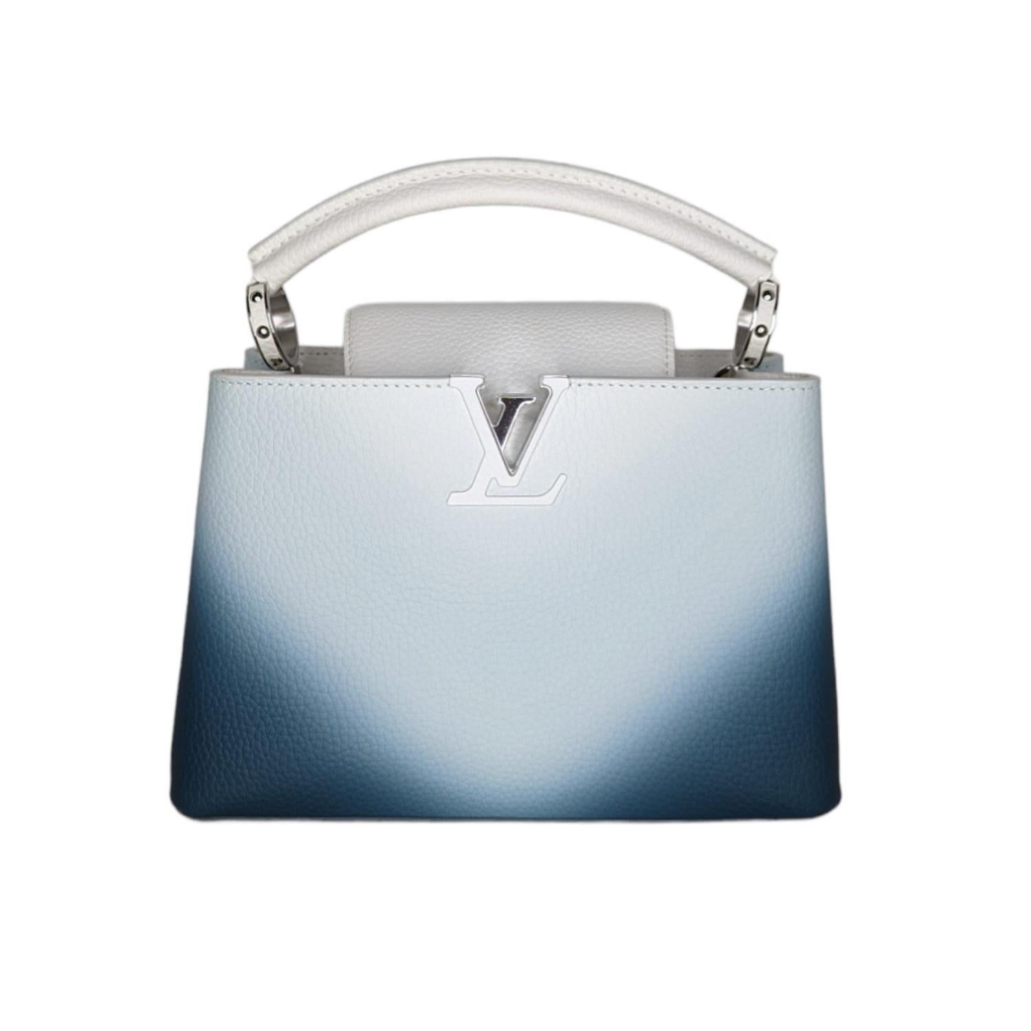 This beautiful bag is composed of luxurious textured calf leather in a white to dark blue ombre. The handbag features a single rolled leather reinforced top handle with stylized links, an optional adjustable shoulder strap, and a crossover flap that