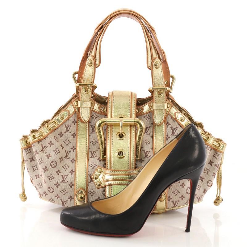 This Louis Vuitton Theda Handbag Mini Lin GM, crafted with beige monogram mini lin, features dual belt straps, cinched side pleats, an oversized top flap buckle design, metallic gold leather trim, and gold-tone hardware. It opens to a beige fabric