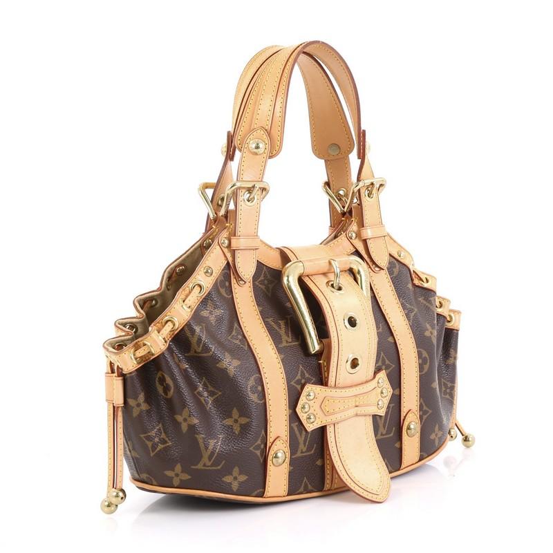 This Louis Vuitton Theda Handbag Monogram Canvas GM, crafted from brown monogram coated canvas, features dual belted straps, oversized adjustable top flap buckle, and gold-tone hardware. Its buckle closure opens to a neutral microfiber interior with