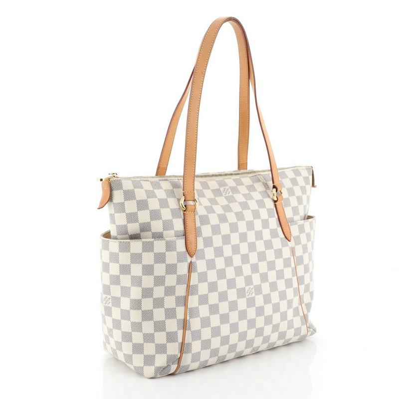 This Louis Vuitton Totally Handbag Damier MM, crafted from damier azur coated canvas, features dual leather handles and trim, two exterior lateral pockets, and gold-tone hardware. Its top zip closure opens to a neutral fabric interior with slip