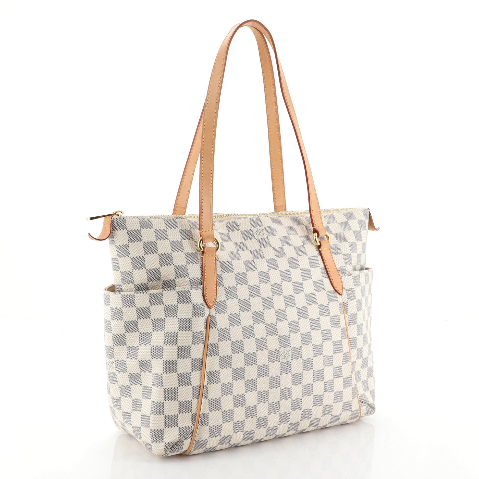 This Louis Vuitton Totally Handbag Damier MM, crafted from damier azur coated canvas, features dual leather handles and trim, two exterior lateral pockets, and gold-tone hardware. Its top zip closure opens to a neutral fabric interior with slip
