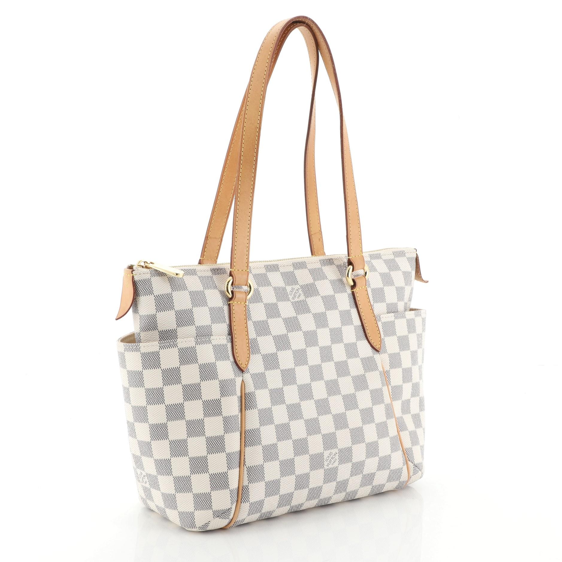 This Louis Vuitton Totally Handbag Damier PM, crafted from damier azur coated canvas, features tall cowhide leather handles and trim, two exterior lateral pockets, and gold-tone hardware. Its top zip closure opens to a neutral fabric interior with