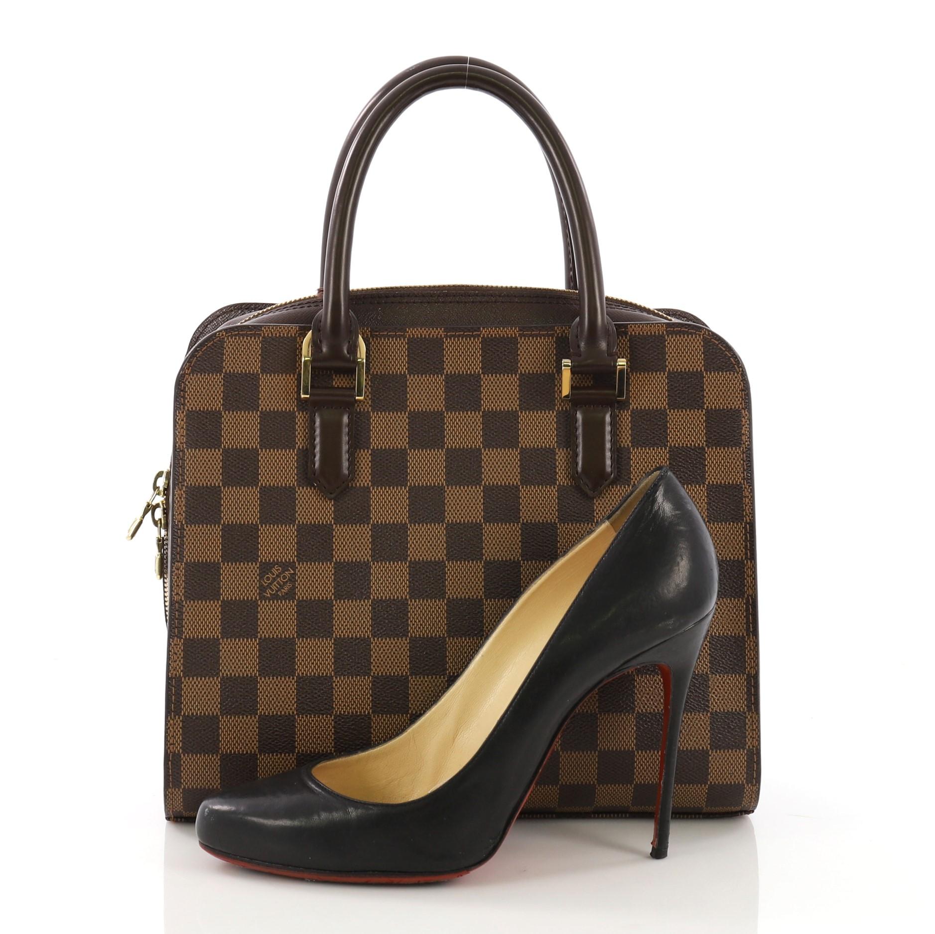 This Louis Vuitton Triana Bag Damier, crafted in damier ebene coated canvas, features dual rolled leather handles and gold-tone hardware. Its zip around closure opens to an orange microfiber interior with zip pocket. Authenticity code reads: VI0044.