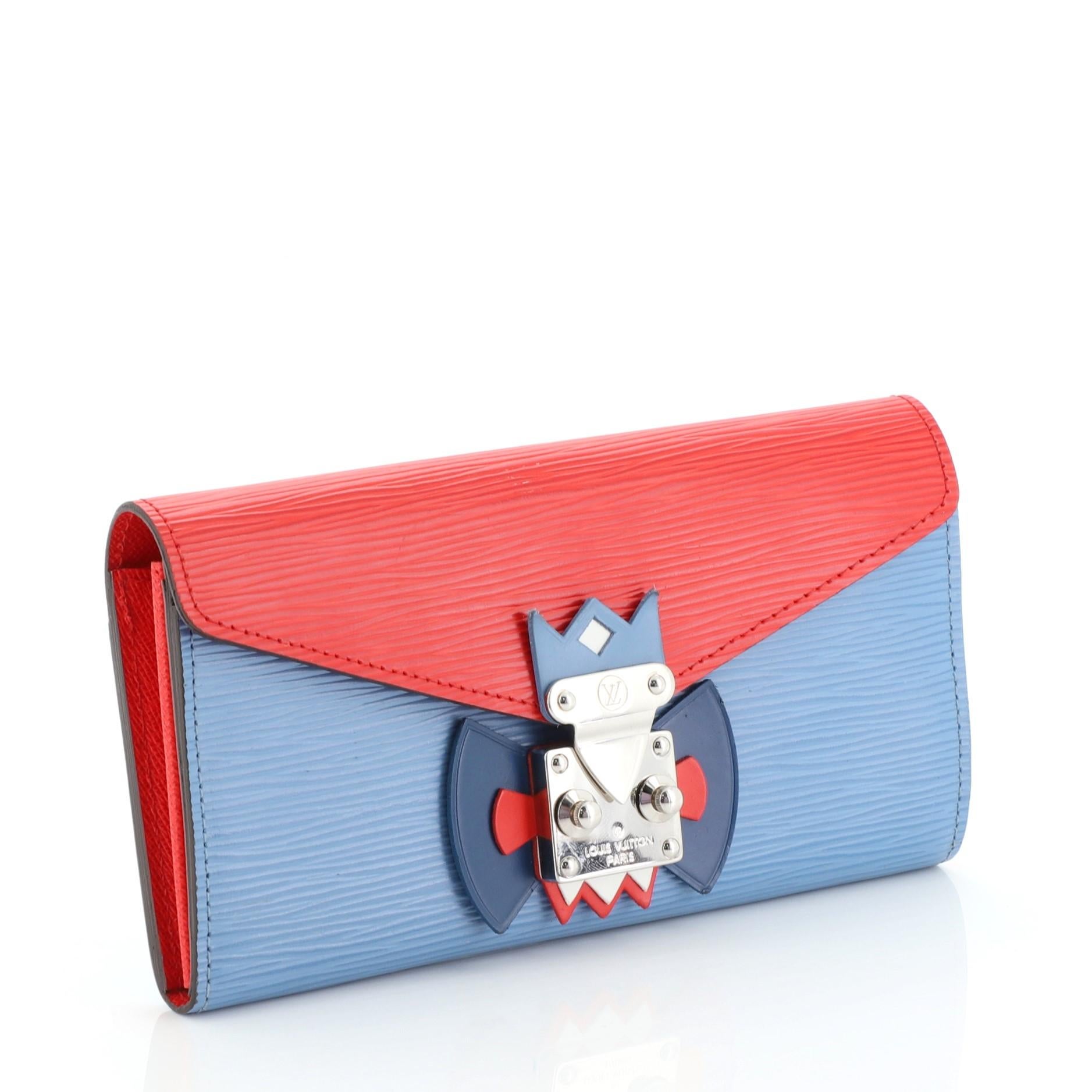This Louis Vuitton Tribal Mask Sarah Wallet Epi Leather, crafted in blue and red epi leather, features tribal mask design on front, envelope shape flap and silver-tone hardware. Its S-lock closure opens to a red leather interior with multiple card