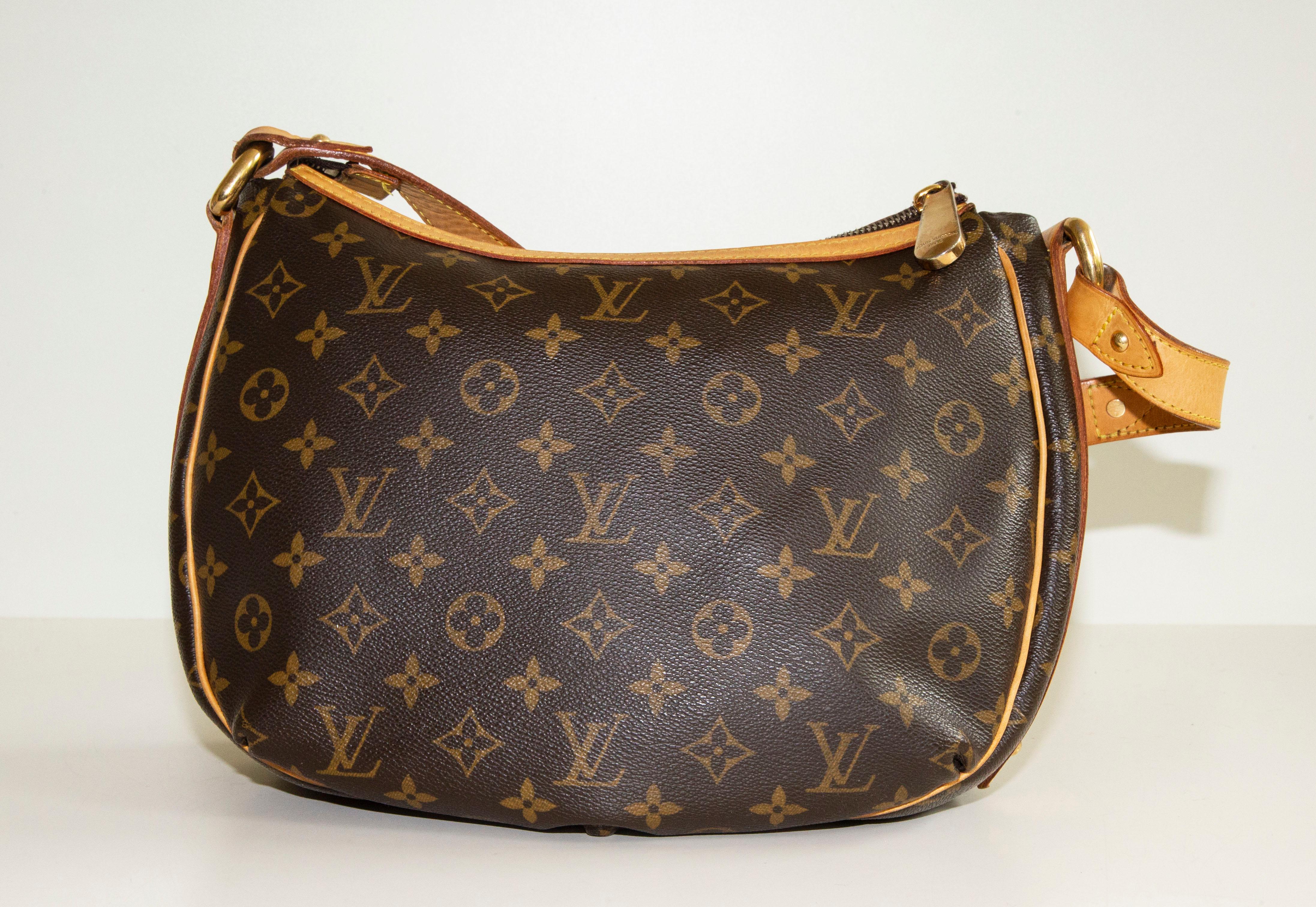 An authentic Louis Vuitton Tulum PM. The bag features an LV monogram coated canvas, light brown leather trim, and gold-toned hardware. The interior consists of the front pocket under the flap and the main compartment. The interior is lined with